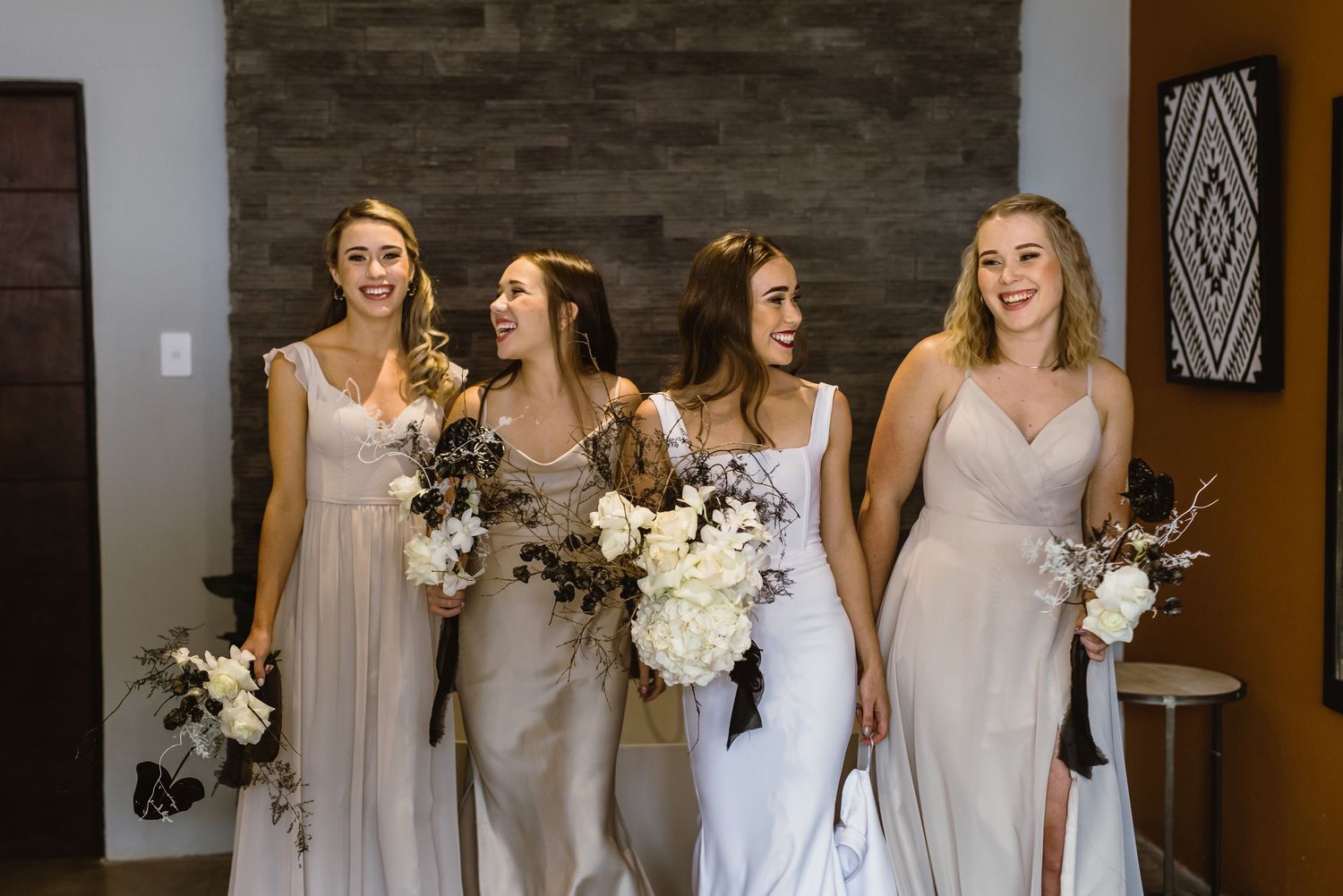 Bridal party in light neutral dresses share joyful moment during wedding preparations.