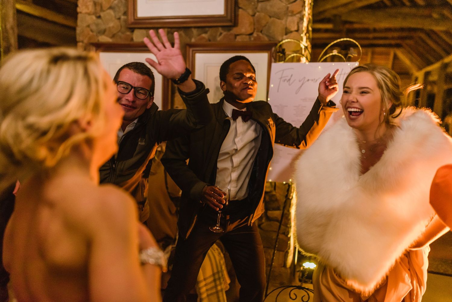 Wedding reception guests dancing and celebrating on a lively dance floor with warm lighting and festive atmosphere.