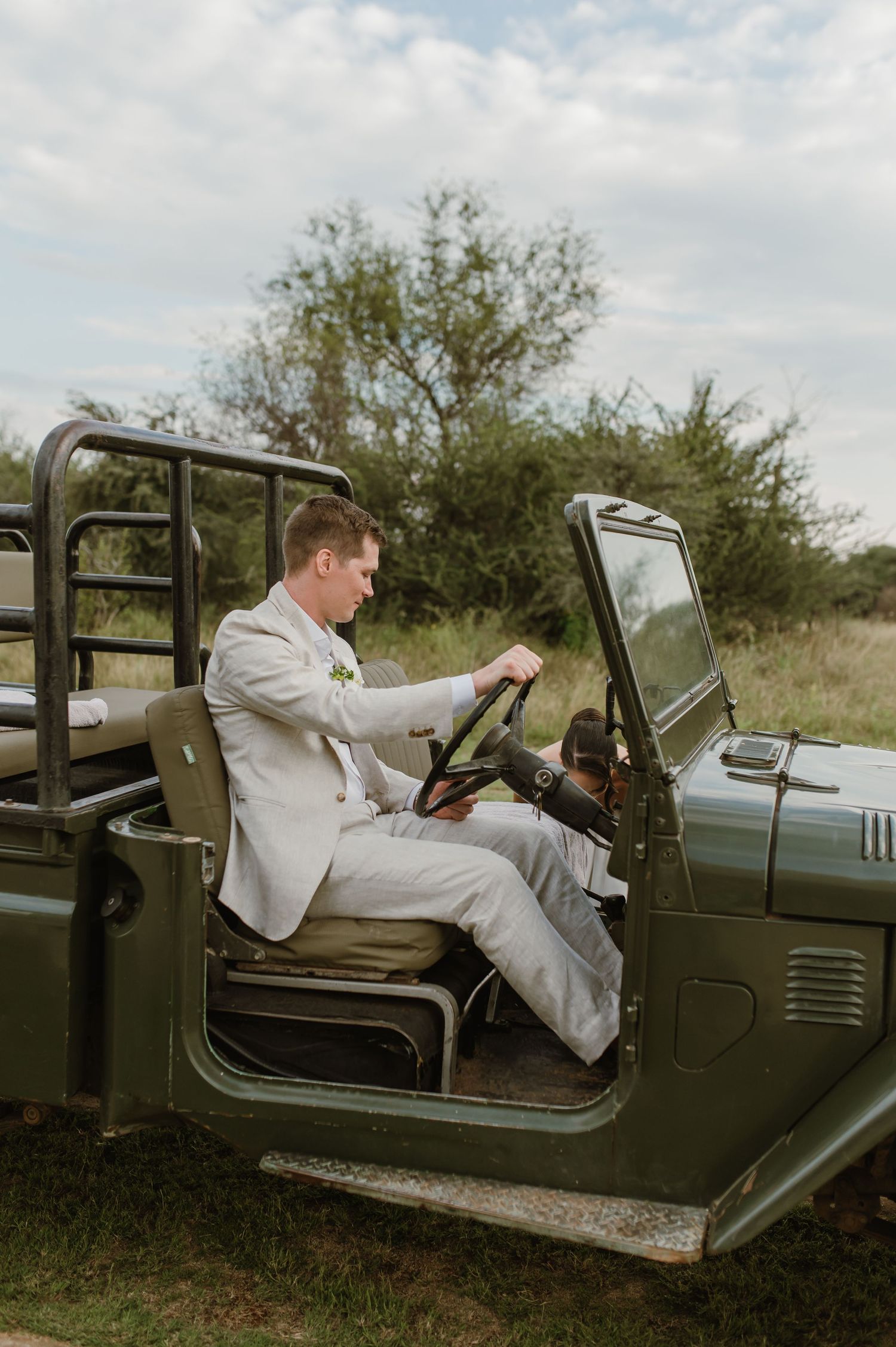 A vintage military-style jeep with someone in formal attire sitting in the driver's seat.