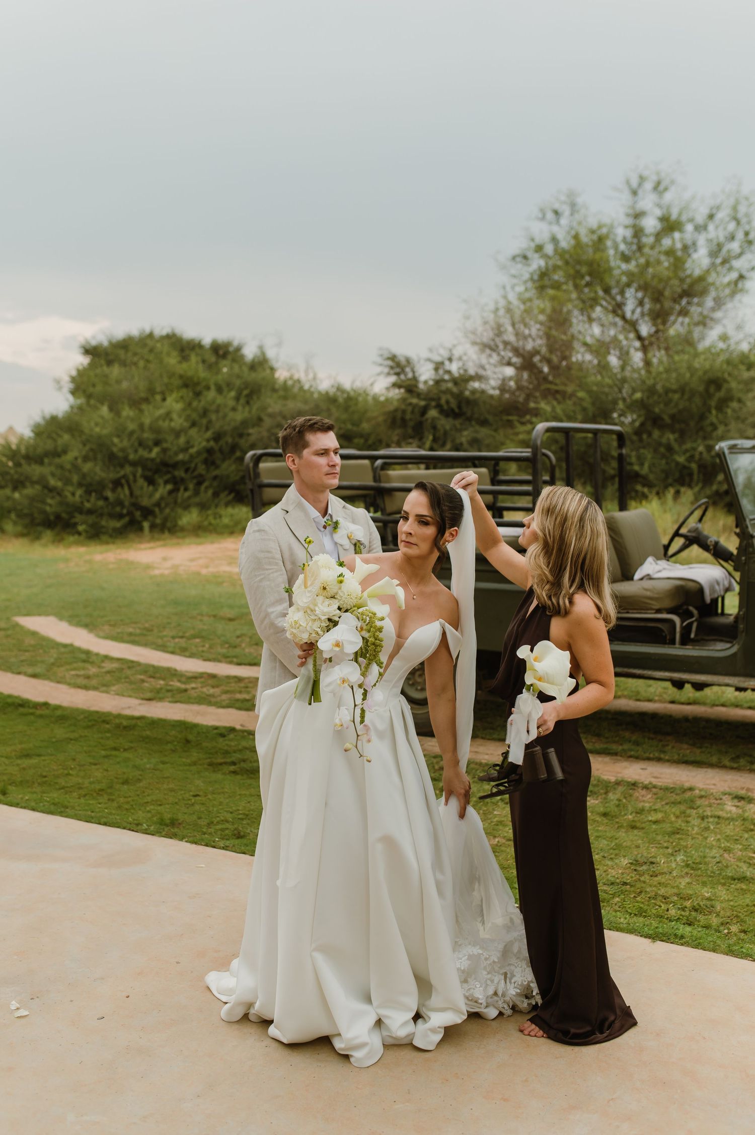 A wedding couple and attendant pose outdoors on a golf course with a golf cart visible in the background.