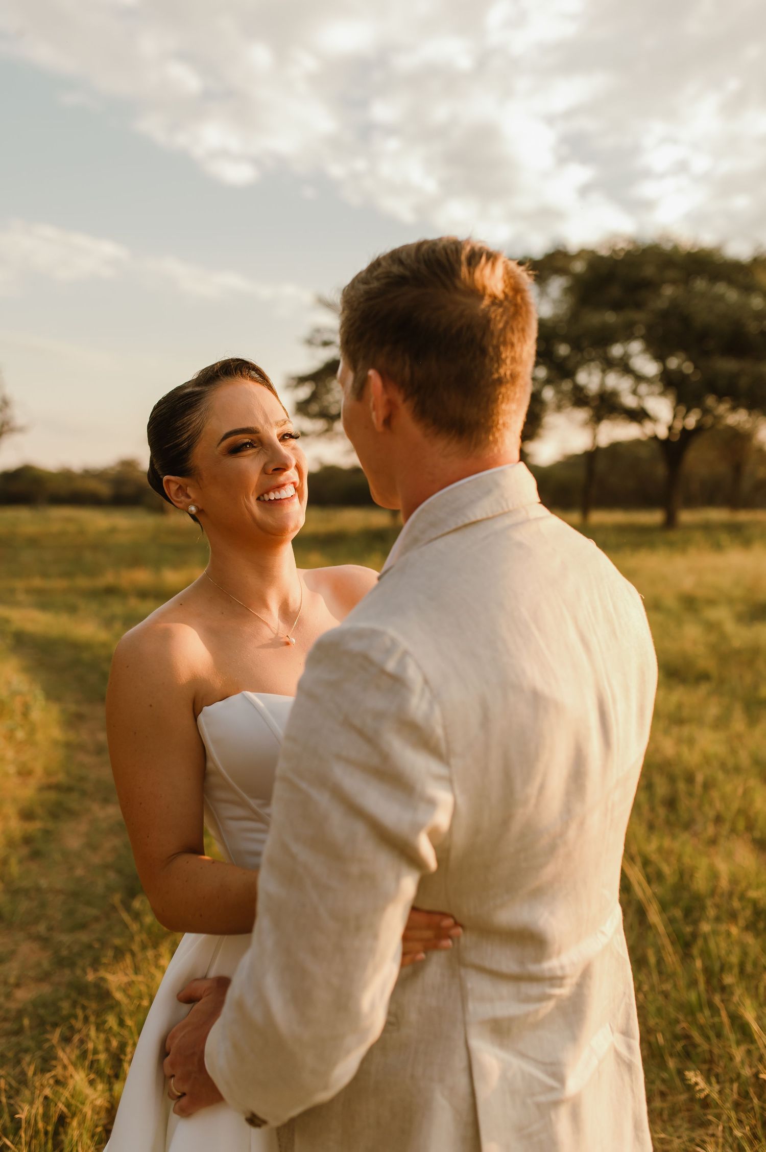 A romantic sunset photoshoot in a golden field with a couple embracing in elegant white attire.
