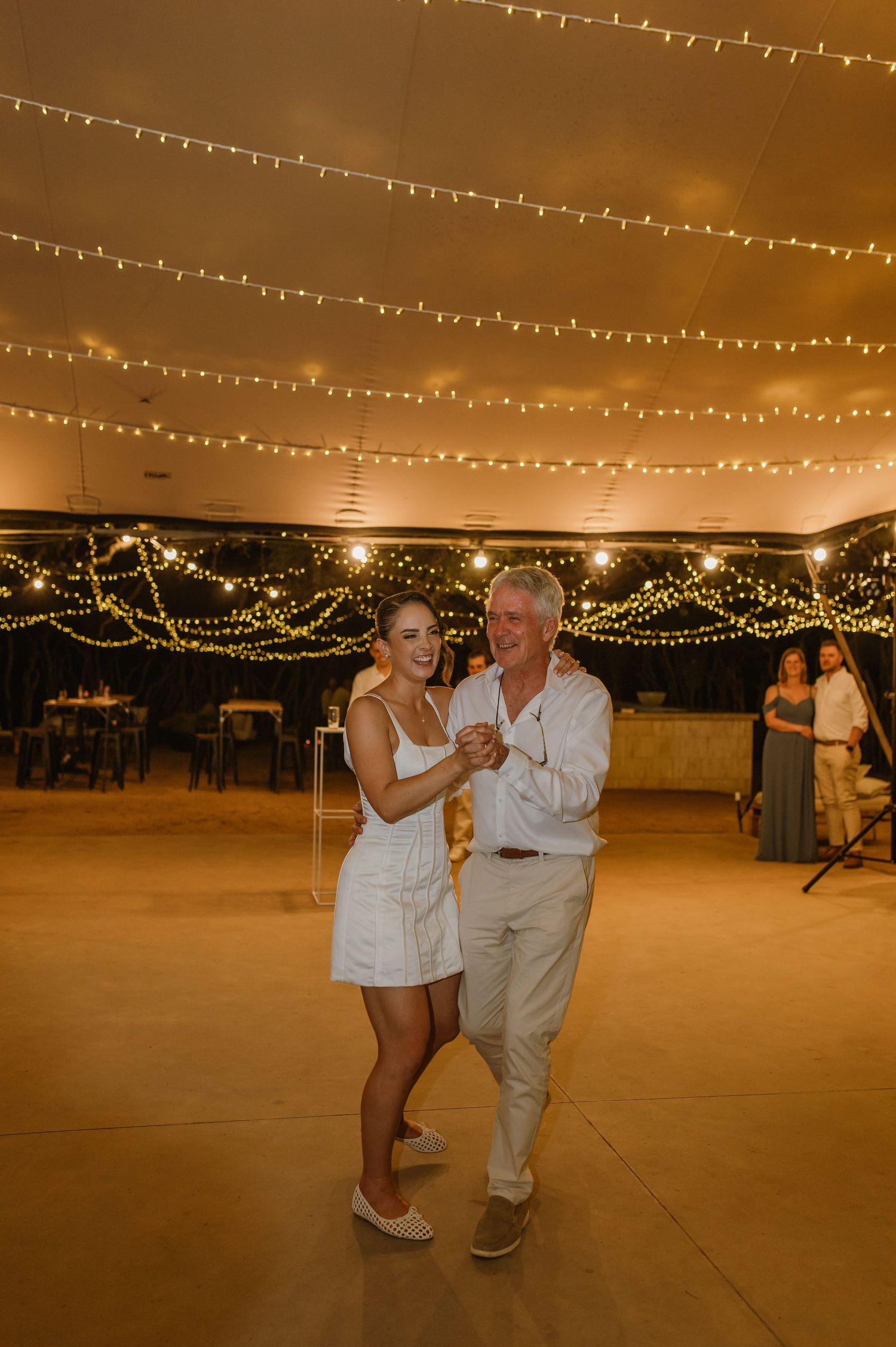 Dancers moving beneath warm string lights at an evening wedding celebration.