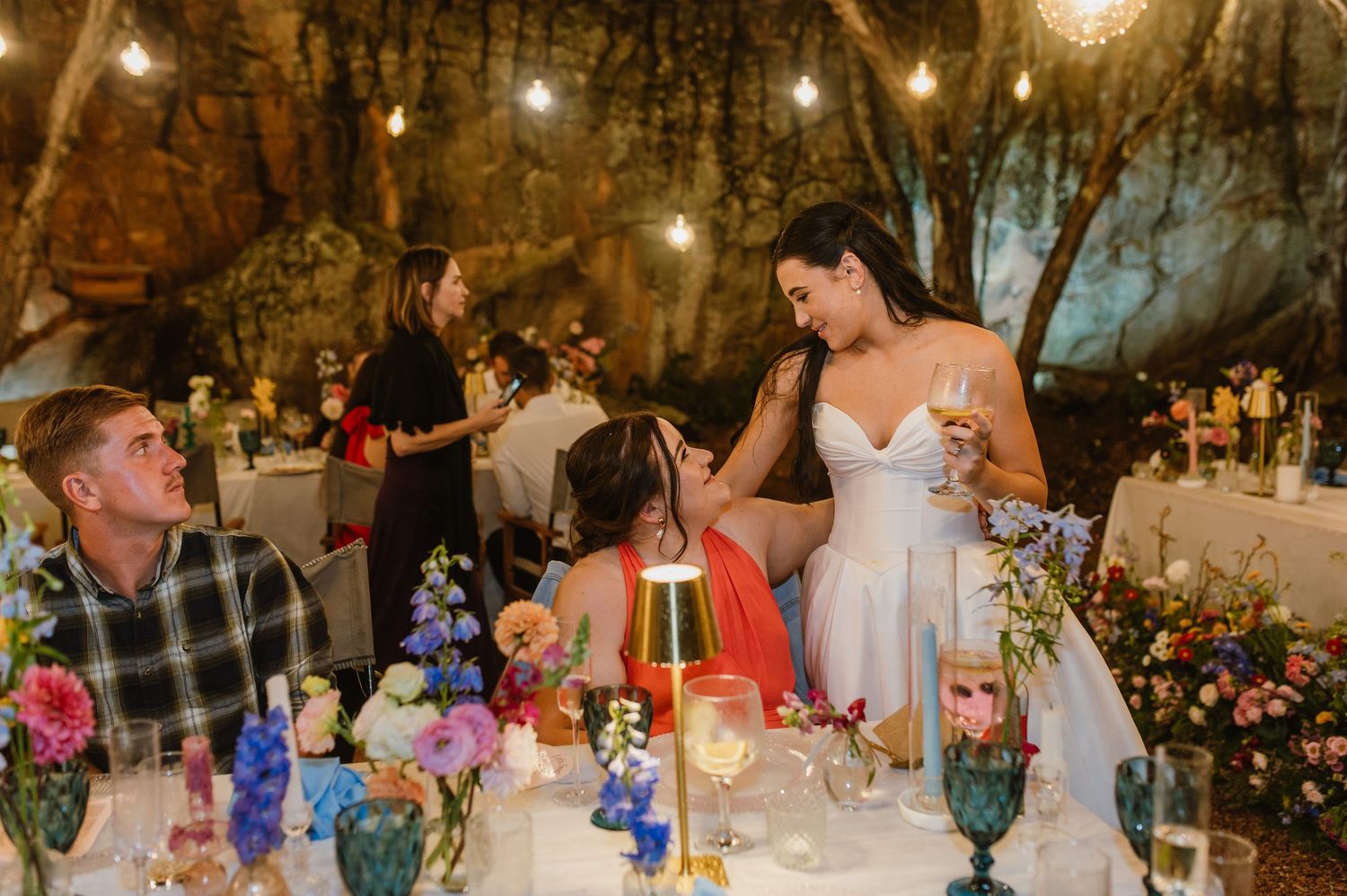 Bride in strapless gown mingles with guests at colorfully decorated wedding reception dinner table.