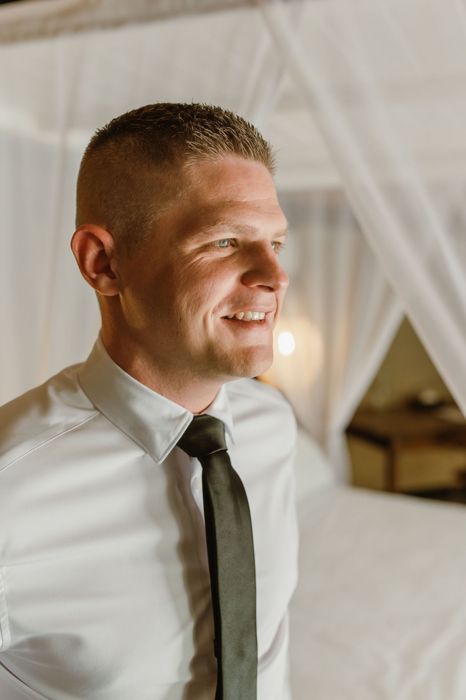 Smiling groom in white shirt and dark tie getting ready for his wedding ceremony.