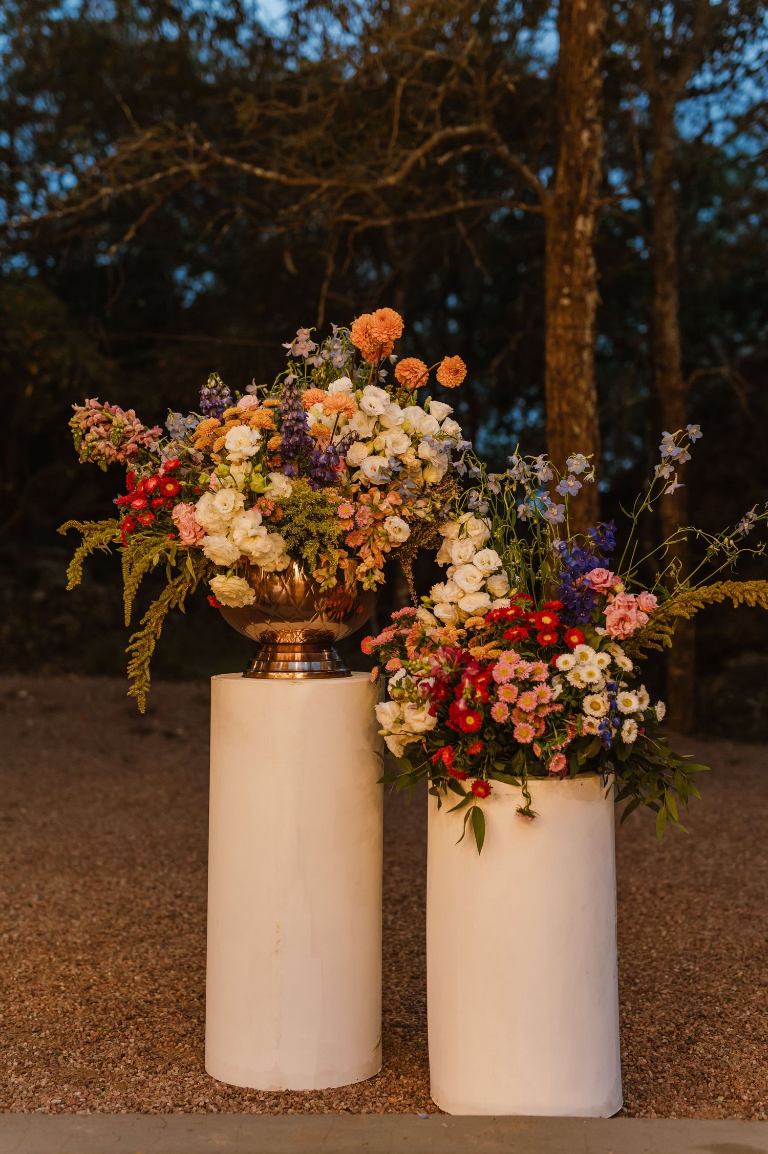 Two white pedestals display lush colorful floral arrangements with roses and wildflowers at wedding.