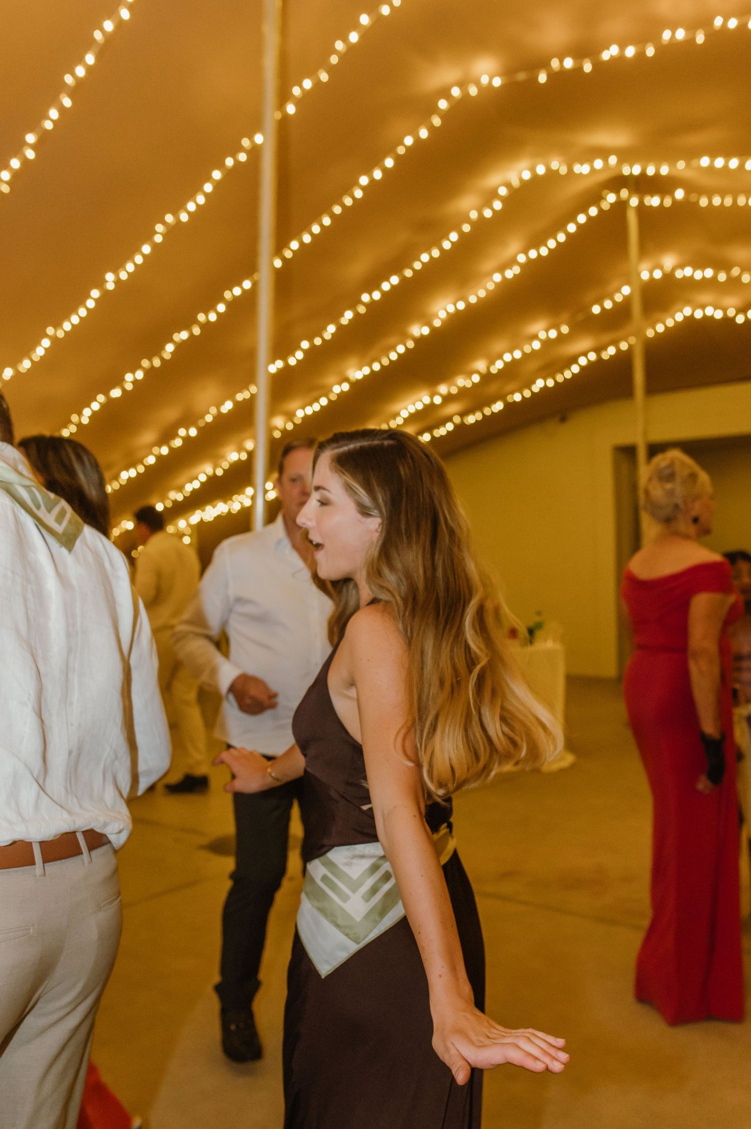 Wedding reception dance floor filled with guests under golden string light decorations.