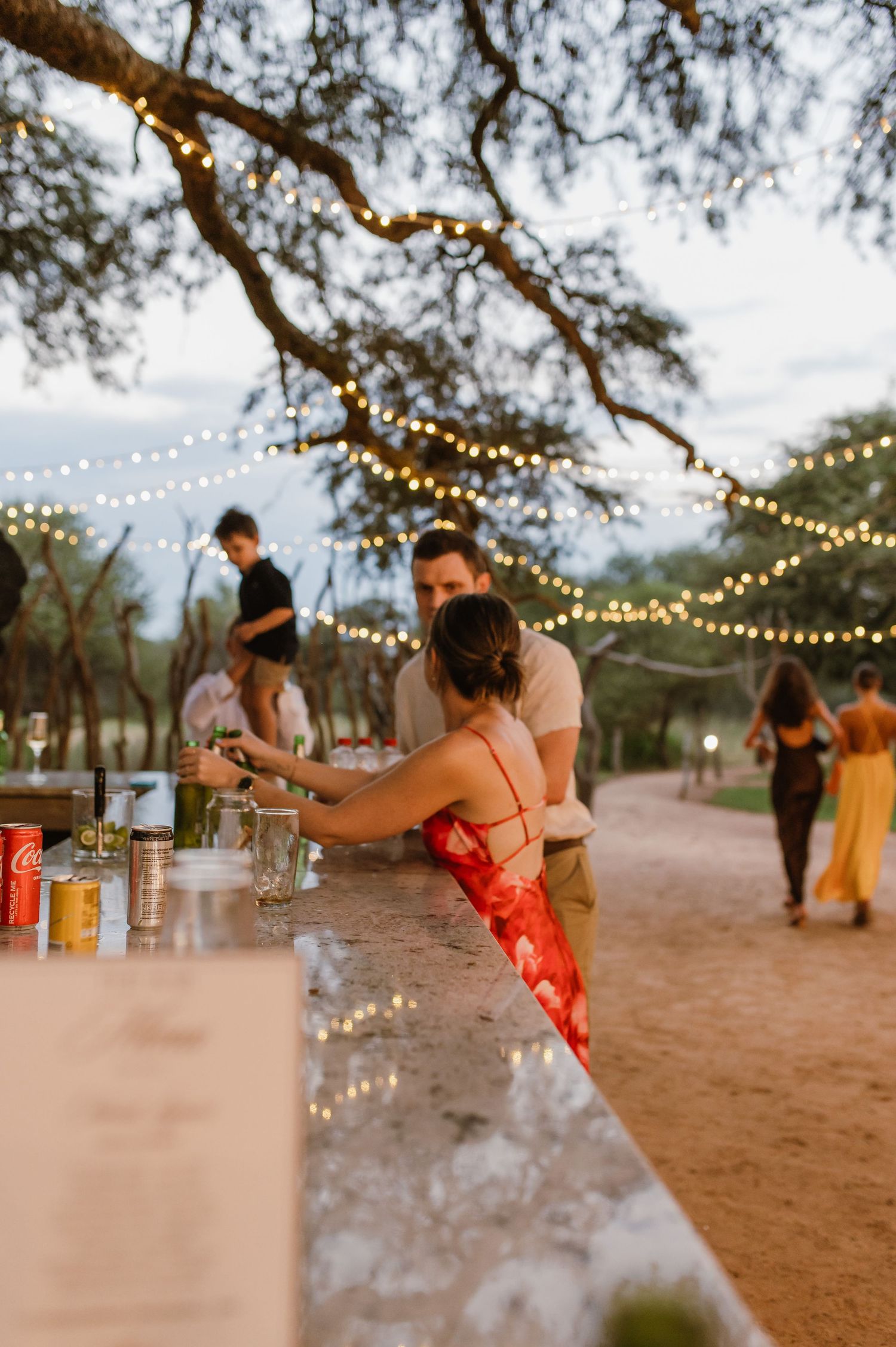Wedding guests dance and celebrate under romantic string lights at an outdoor desert reception venue.