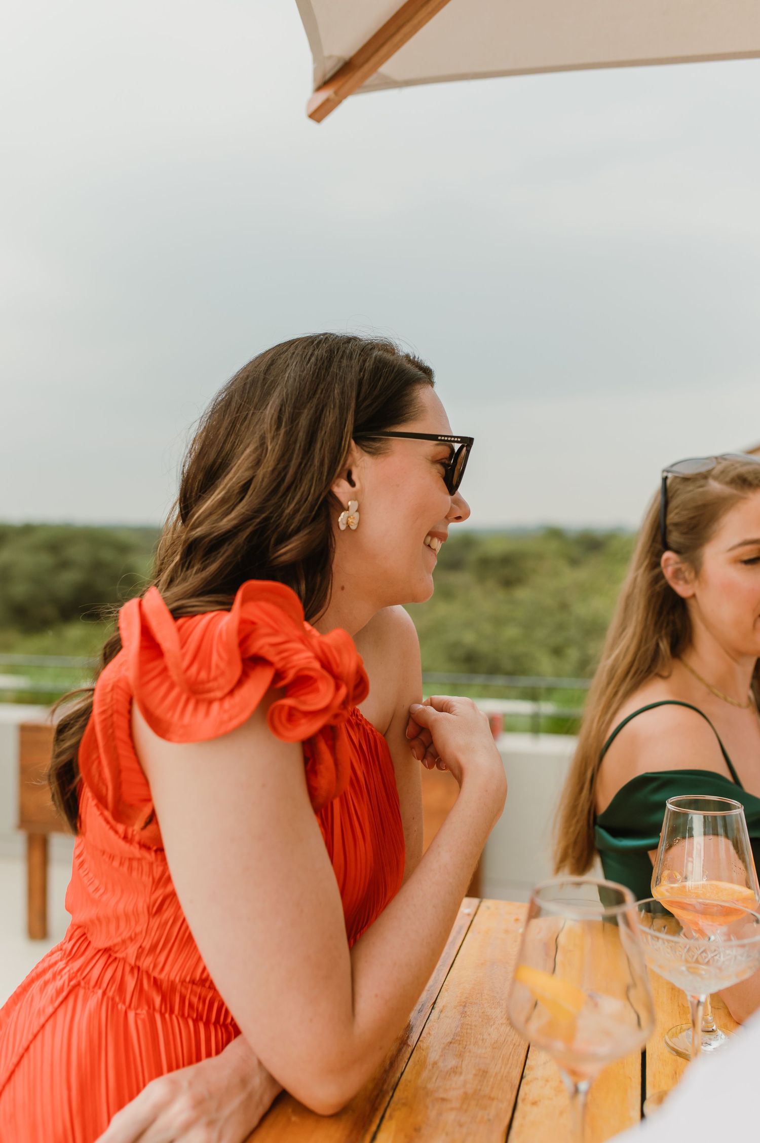 Friends enjoying drinks and laughter at an outdoor party under white umbrellas.