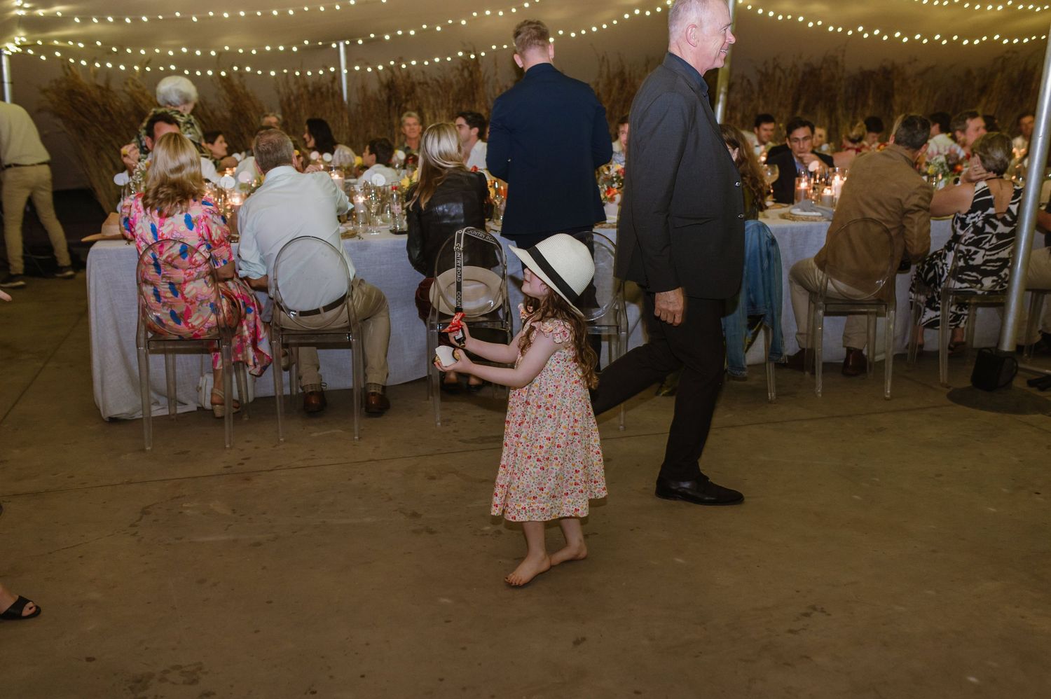 String lights illuminate a rustic indoor wedding reception venue with dancing guests.