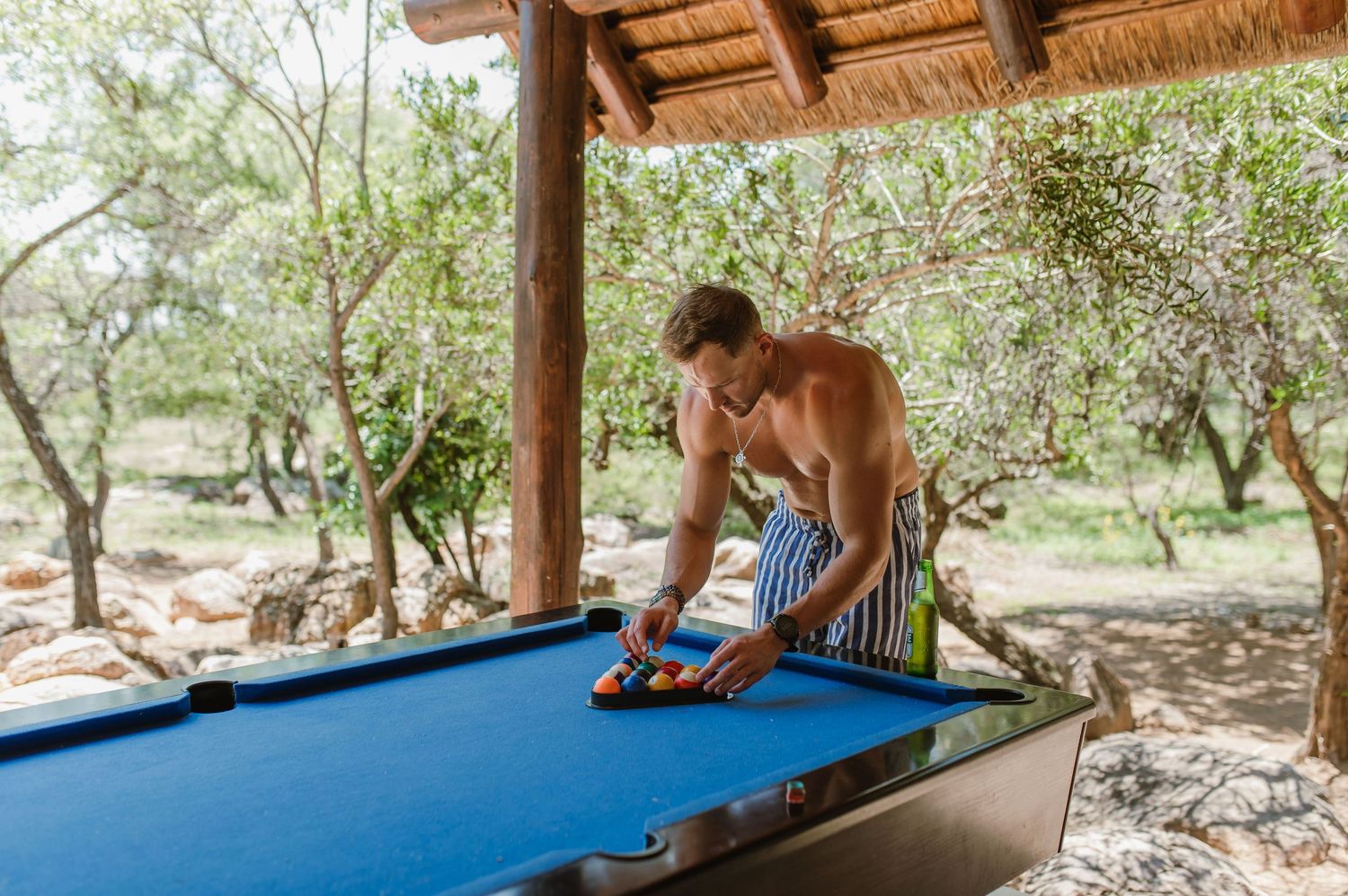 Pool game in progress under a rustic thatched-roof structure with natural lighting.