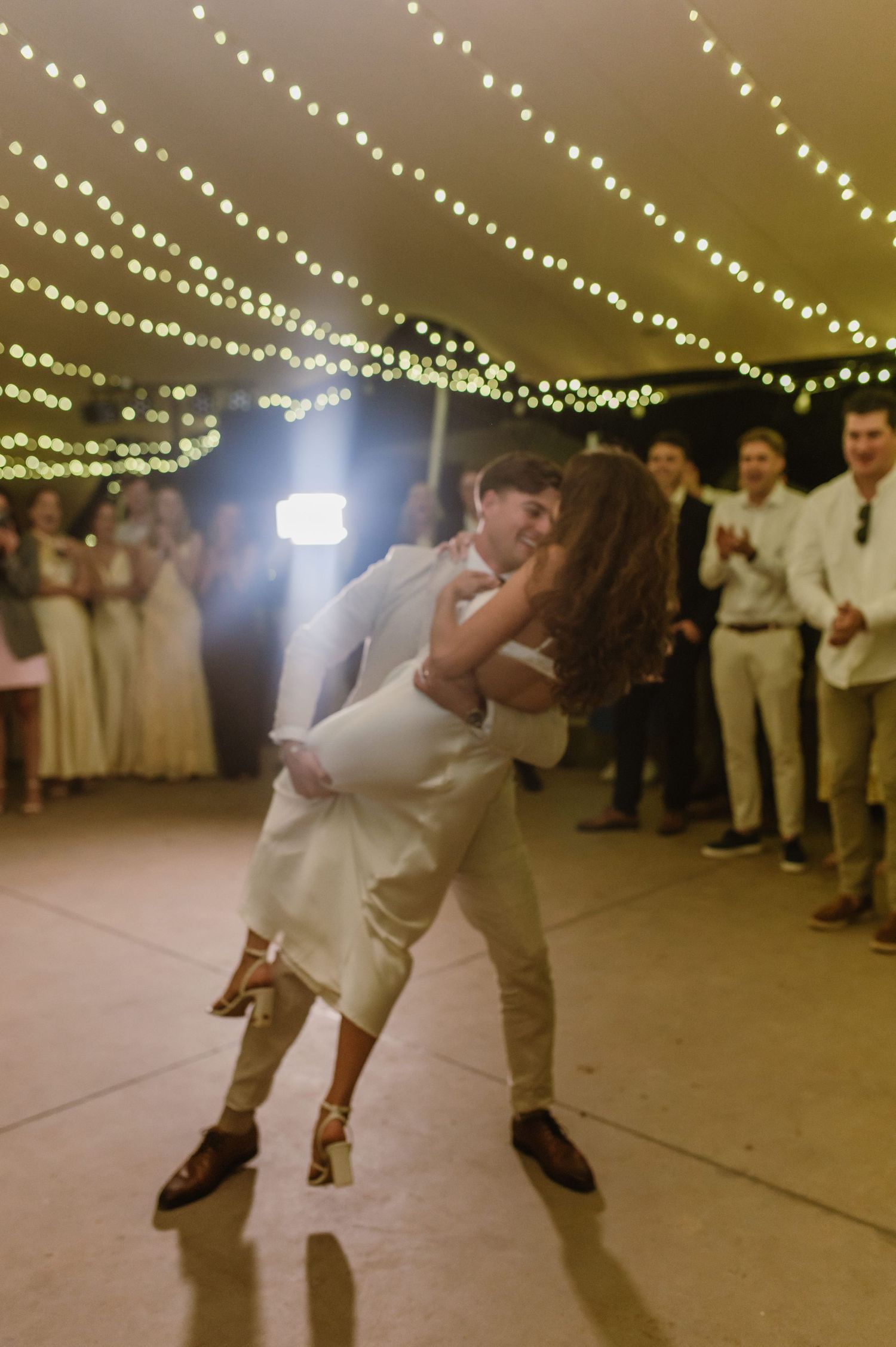 A romantic dip during the wedding dance under string lights with guests watching.