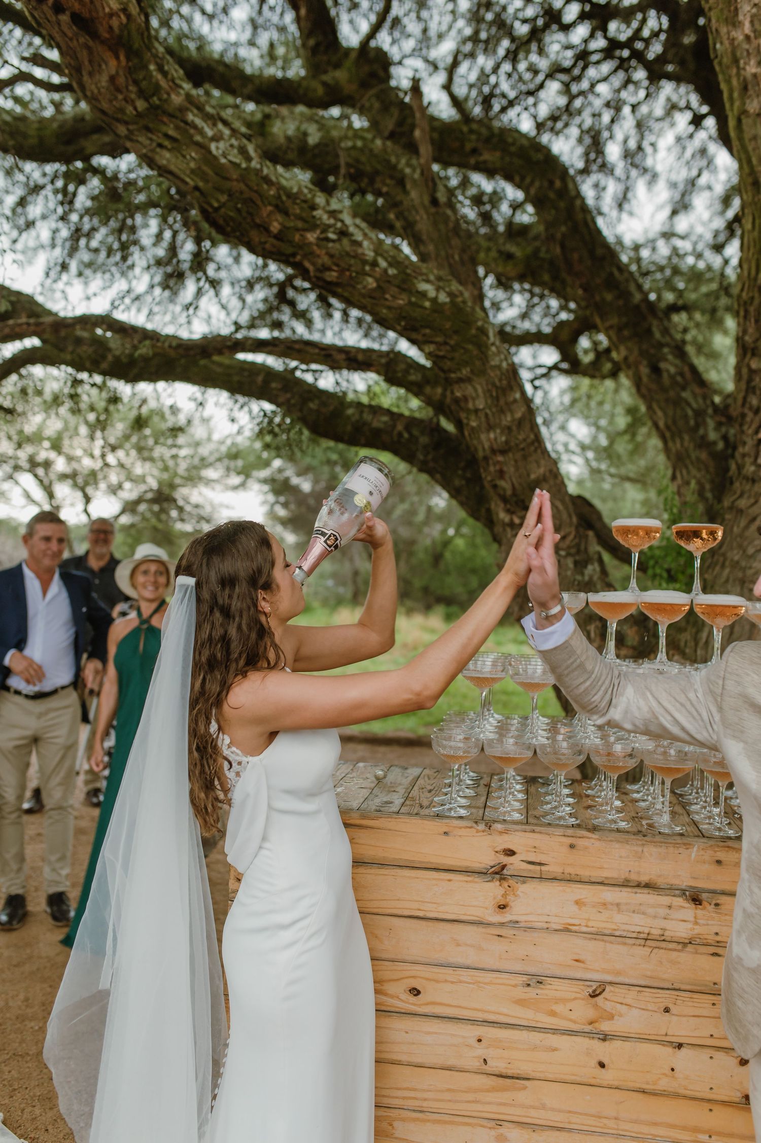 Wedding guests performing a champagne tower pour at an outdoor reception.