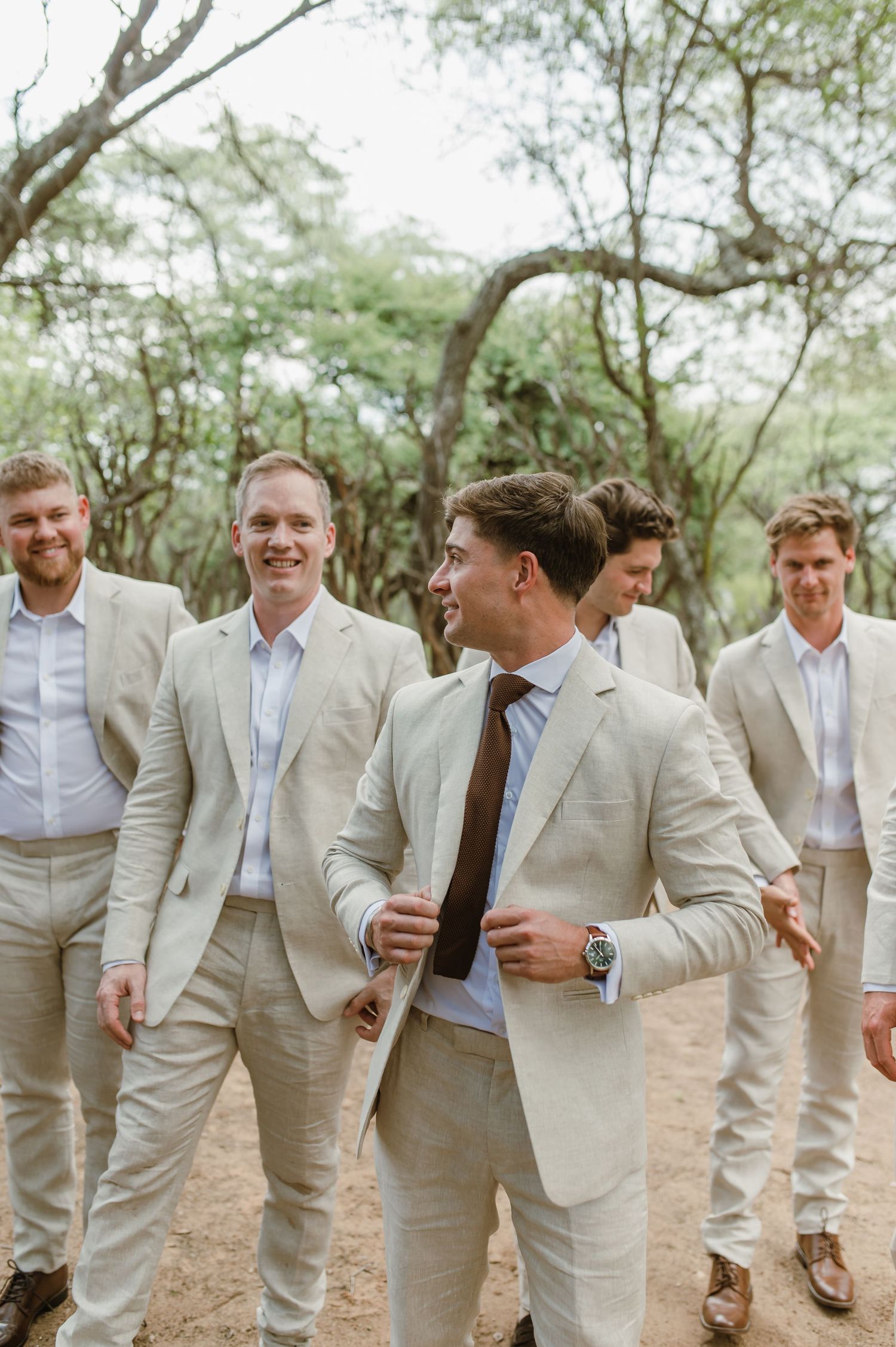Groomsmen in matching suits share laughs and candid moments in a wooded setting.