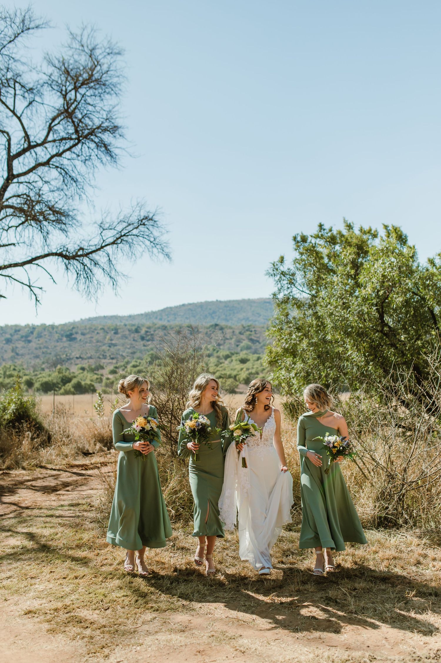 Wedding group stands together on desert path with mountains and blue sky in background.