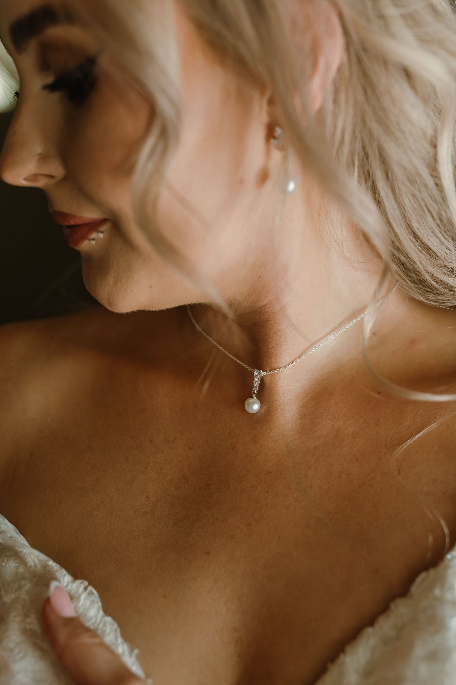 Close-up detail shots of delicate pearl drop earrings and neckline jewelry on a bride.