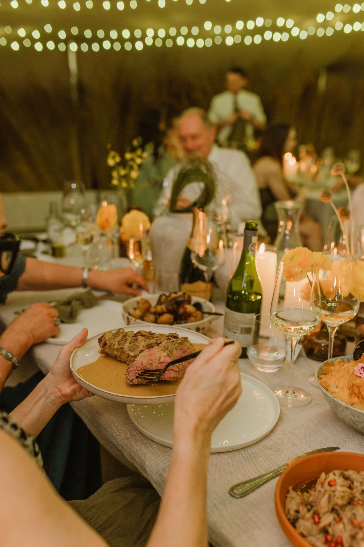 Elegant wedding dinner table setting with candles and shared plates under string lights.