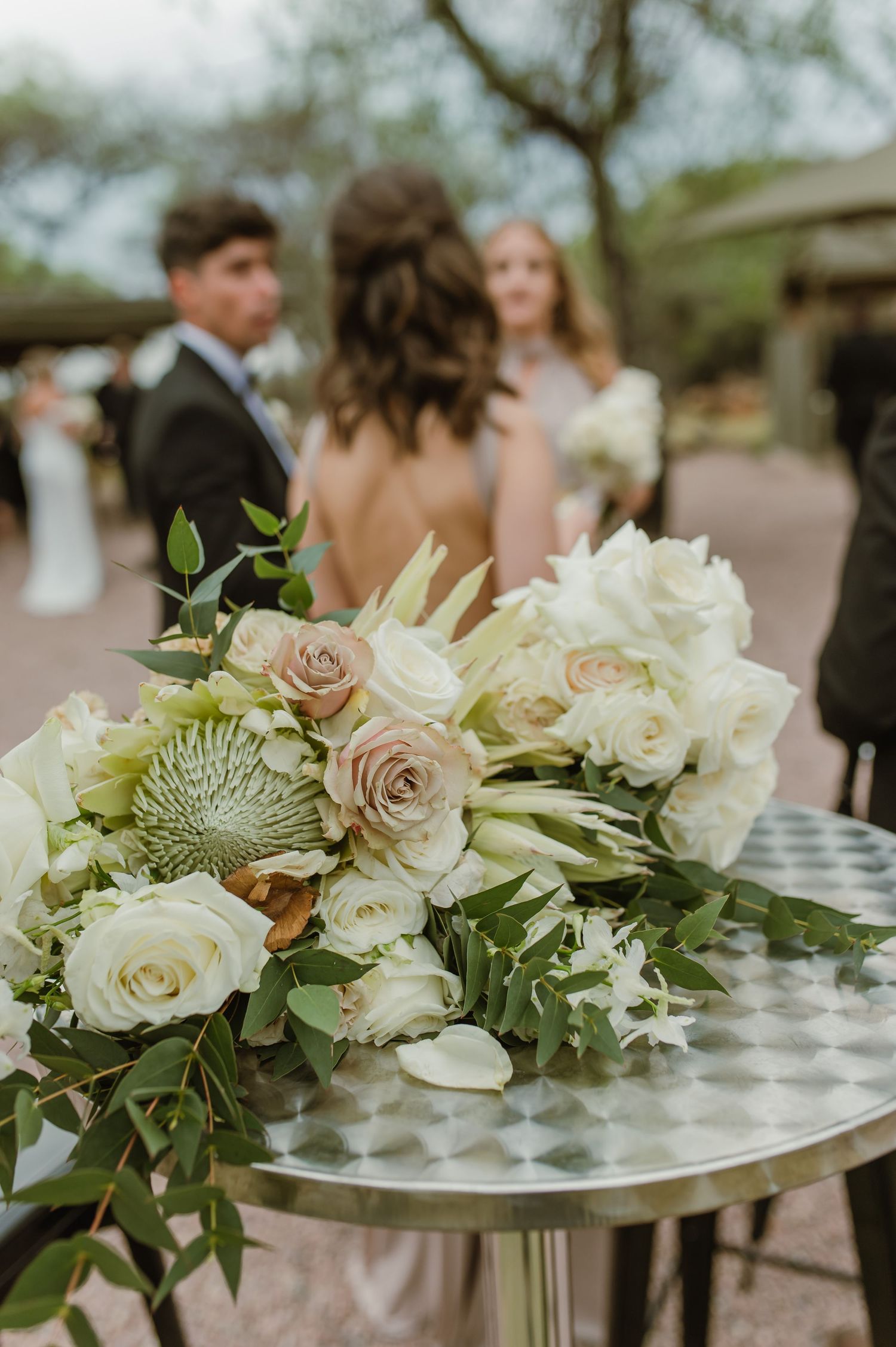Elegant floral centerpiece with white roses and greenery on silver table at wedding reception.