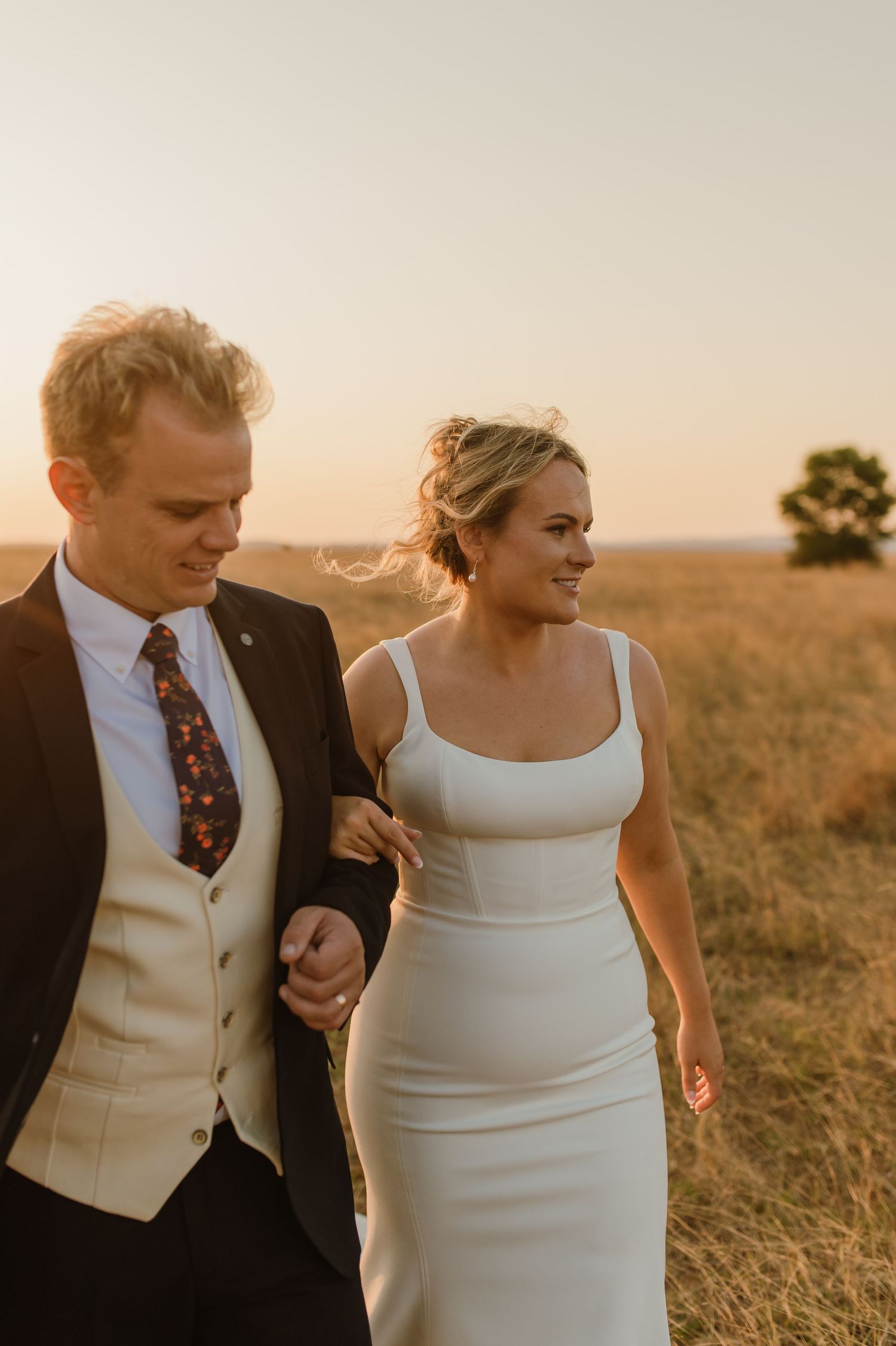 Couple walking together through golden field during sunset wedding shoot.