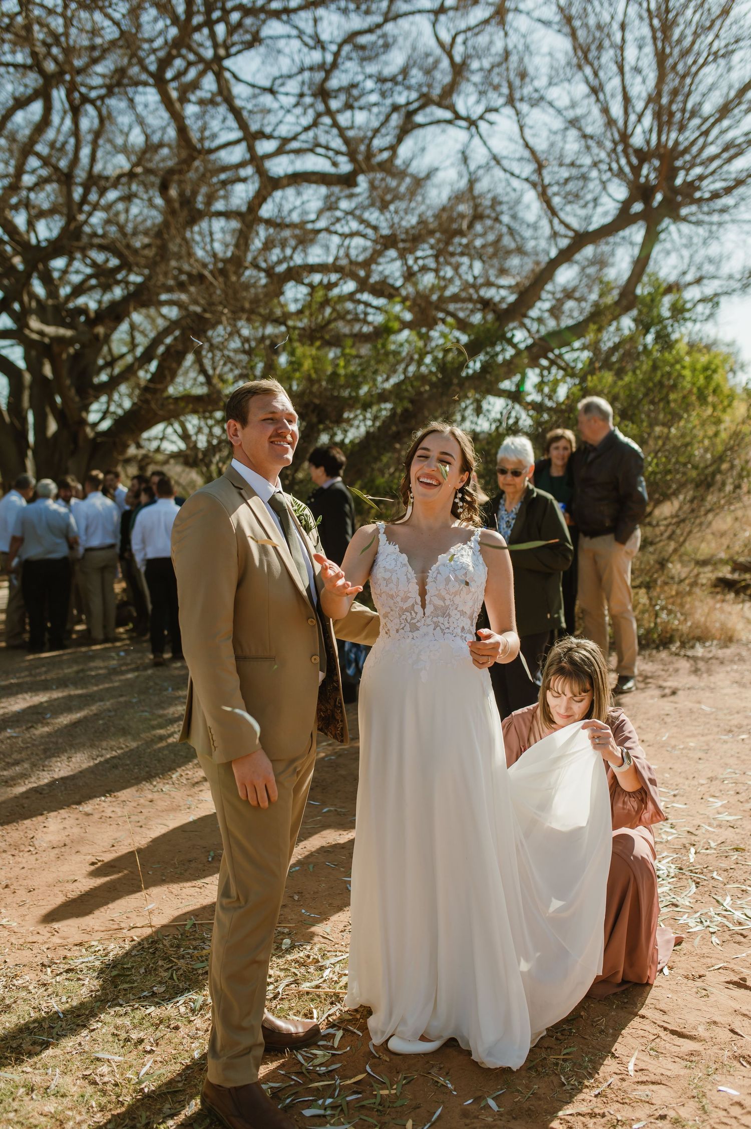 Outdoor wedding scene with guests celebrating under a canopy of twisted branches.