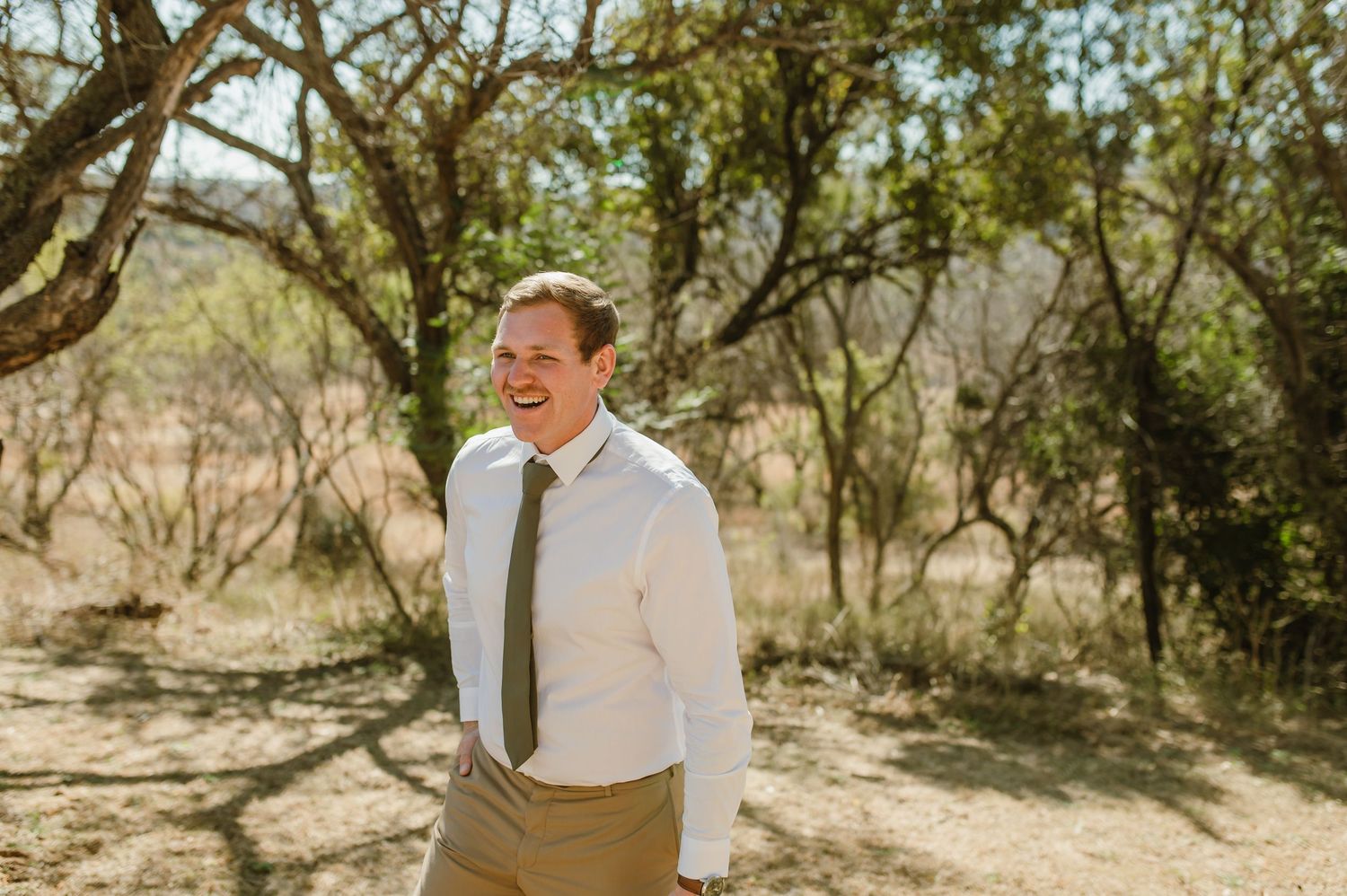 Wedding party members in light colored attire pose against natural African landscape.