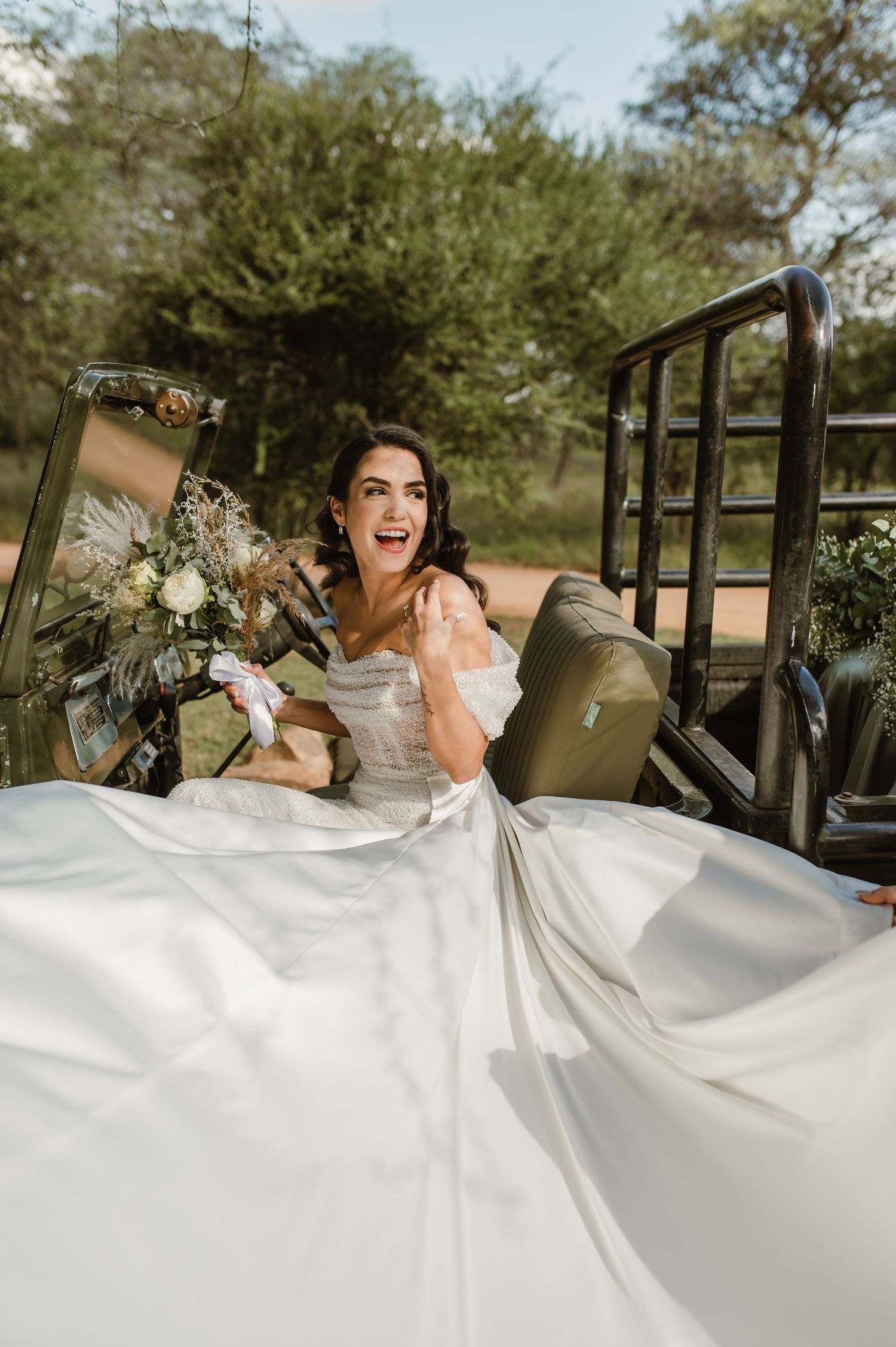 Dramatic bridal portrait with flowing white dress against vintage military vehicle backdrop.
