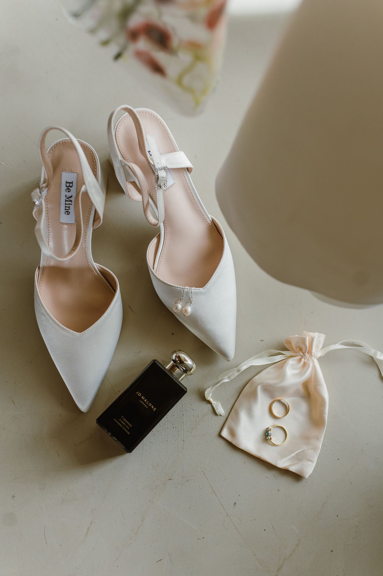 Elegant white bridal shoes with slingback straps and a small jewelry pouch on a light surface.