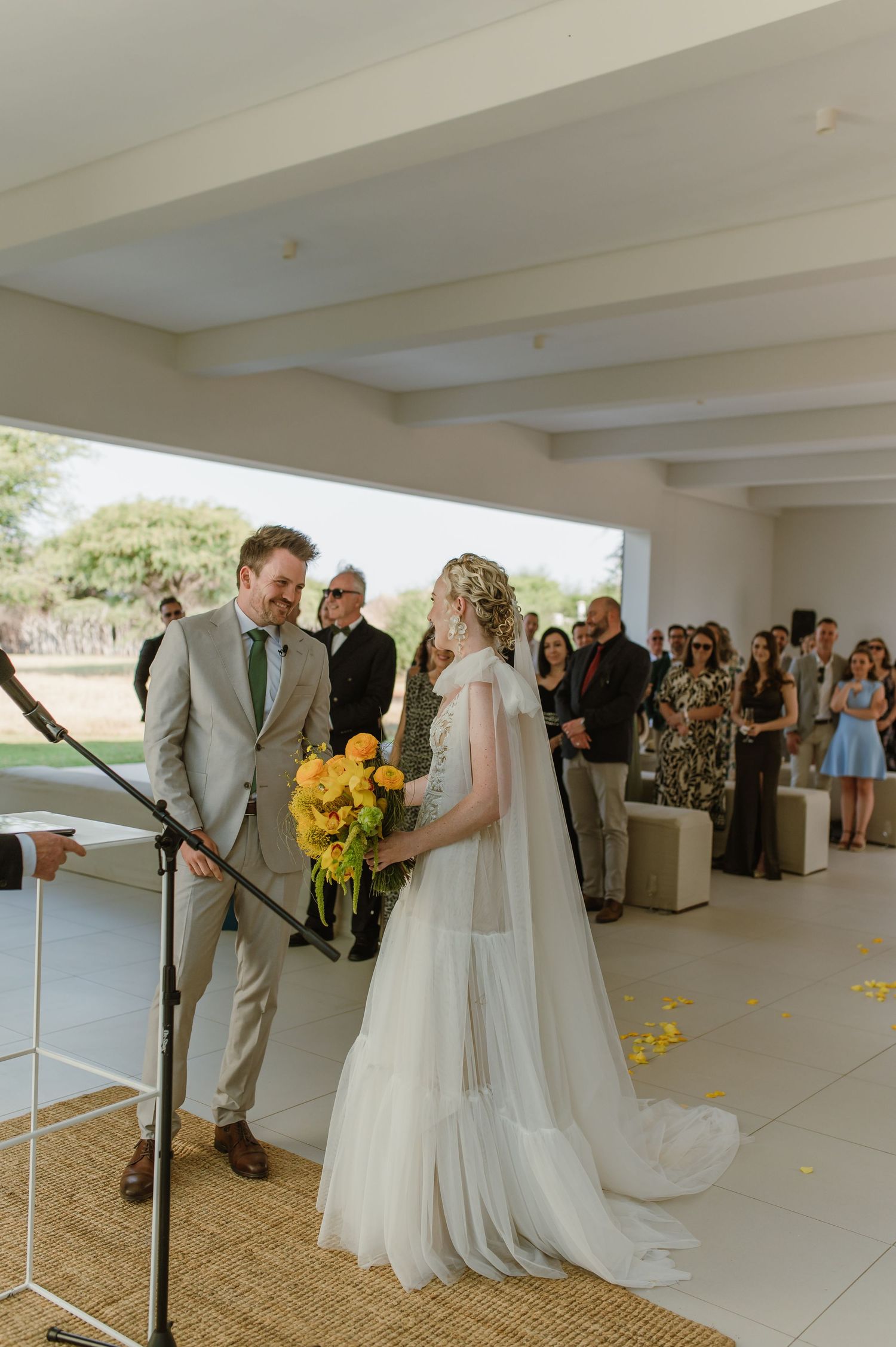 Wedding ceremony underway in modern white venue with desert landscape visible through windows.