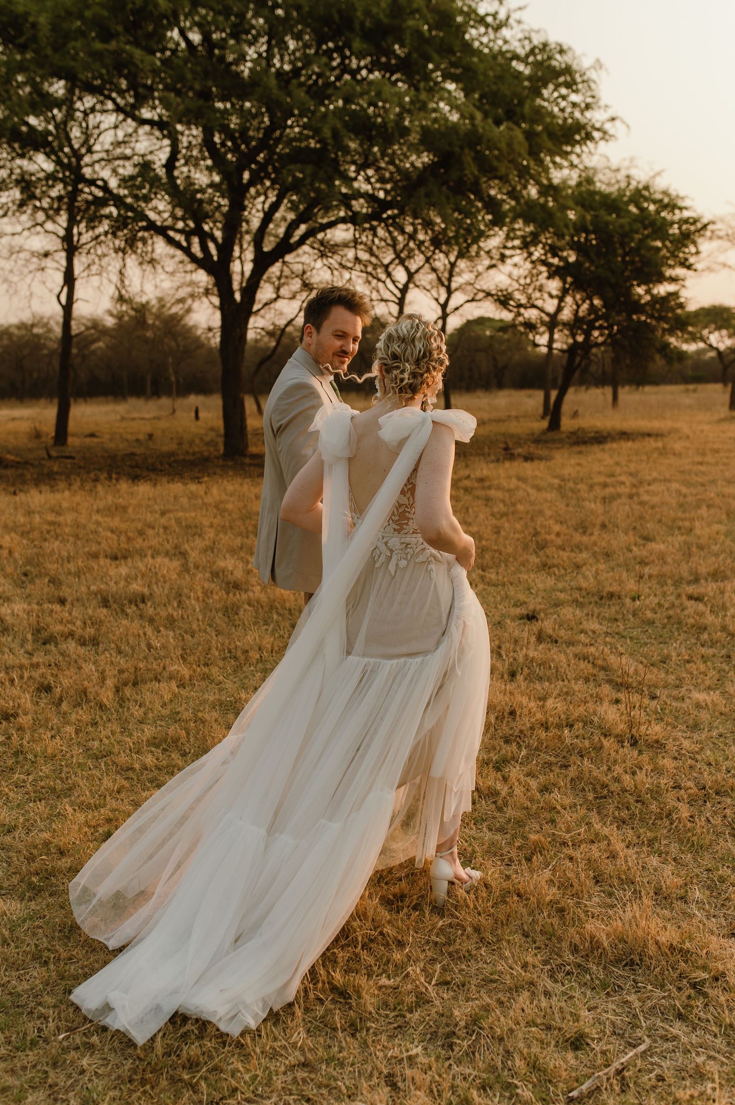 A romantic wedding portrait showing flowing white dress details against a warm sunset backdrop.