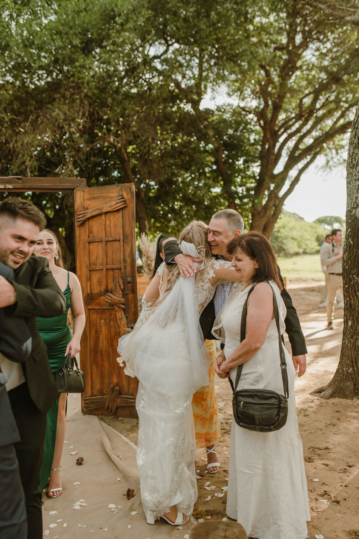 Wedding party exits through rustic wooden doors in outdoor setting.