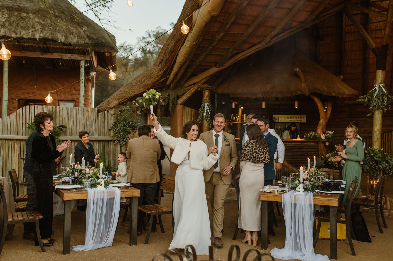 Wedding reception setup in a rustic wooden barn with hanging lights and elegant table settings.