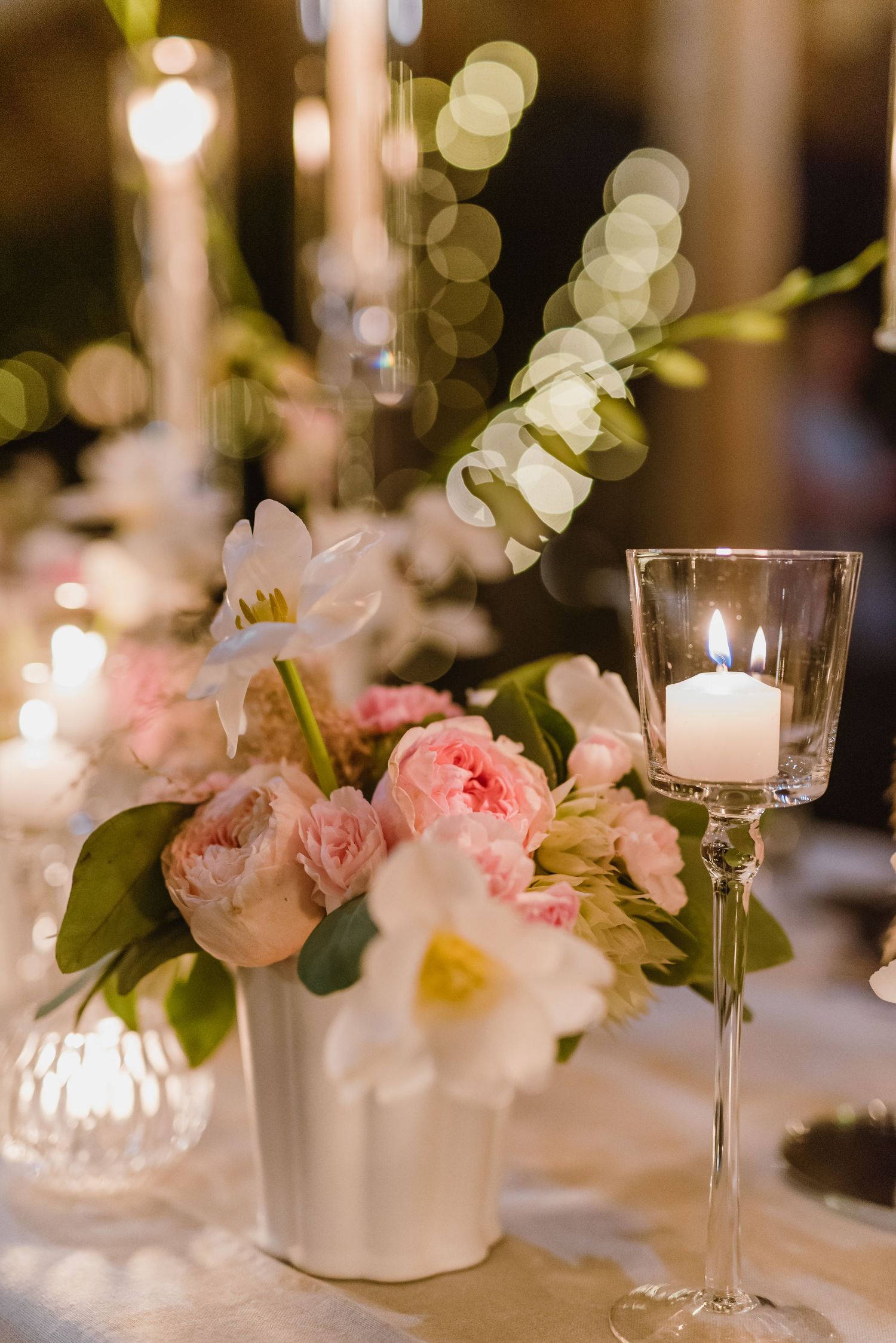 Pink garden roses and white candles create an elegant table setting with soft bokeh lighting effects.