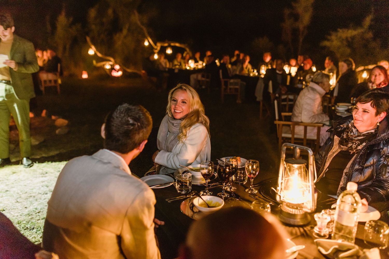 Intimate outdoor dinner party with lanterns and candlelight creating a warm atmosphere.