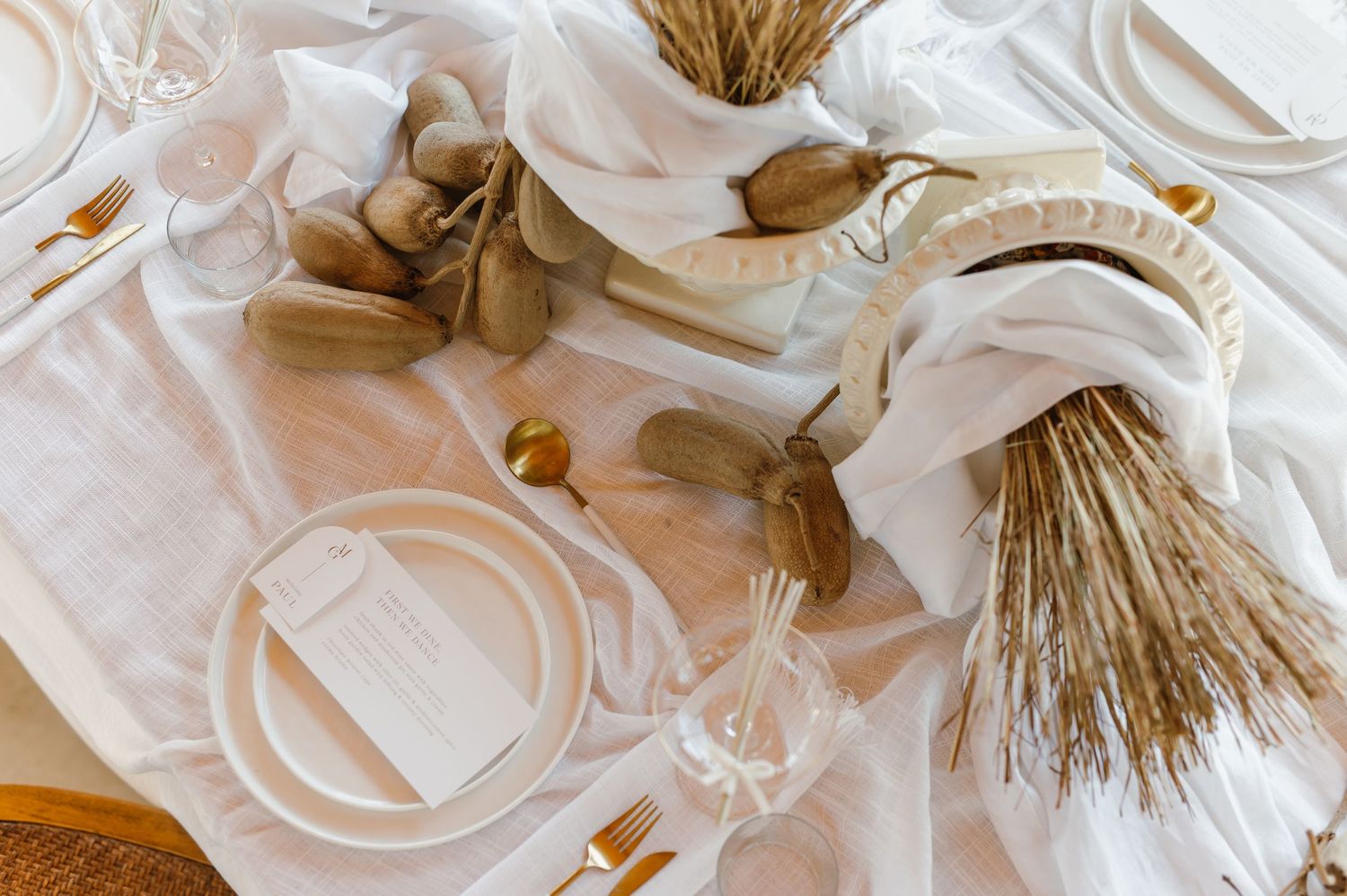 Wedding table decor with dried wheat bundles and white linens creating a rustic elegant atmosphere.