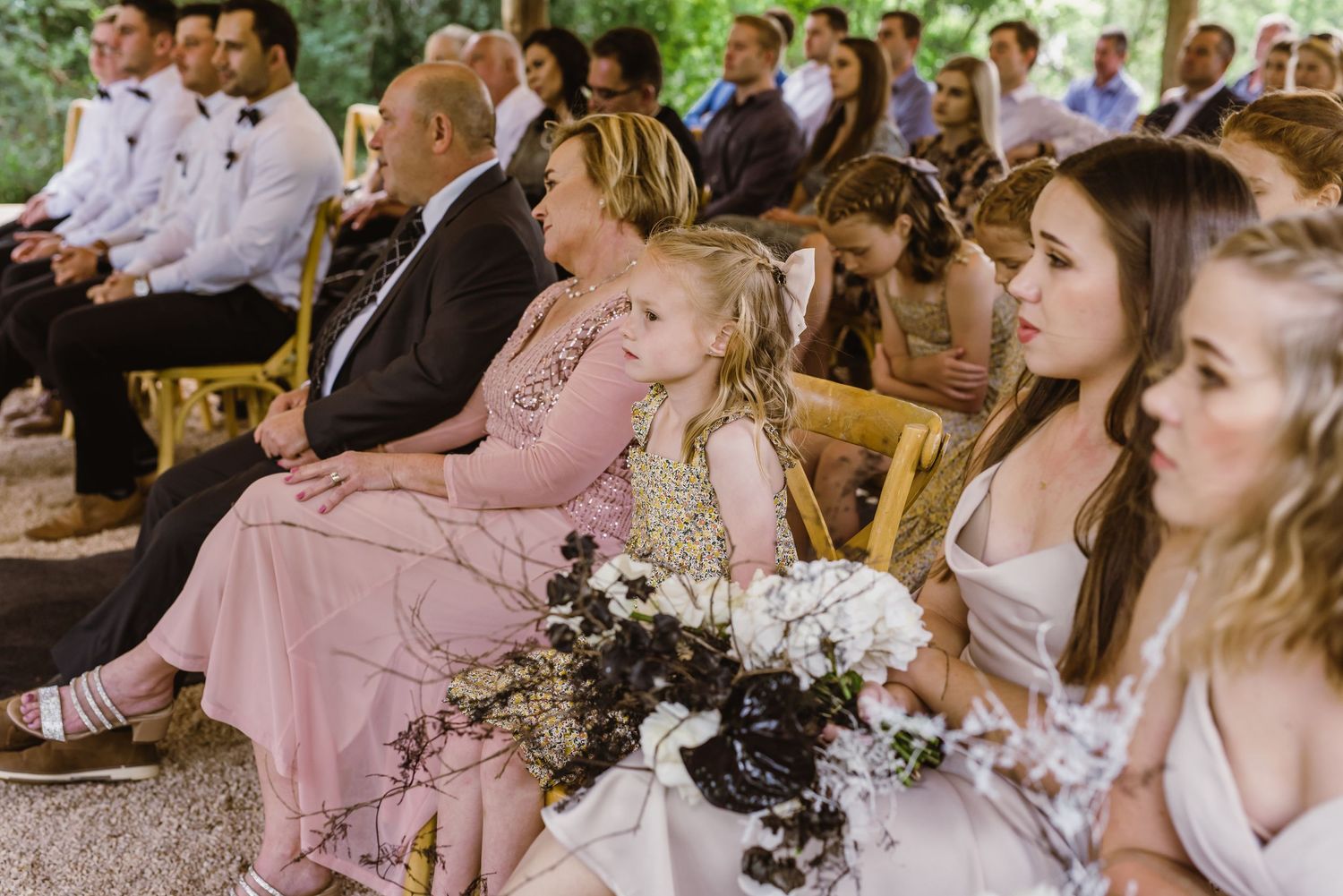 Wedding guests react emotionally during an outdoor ceremony under trees.