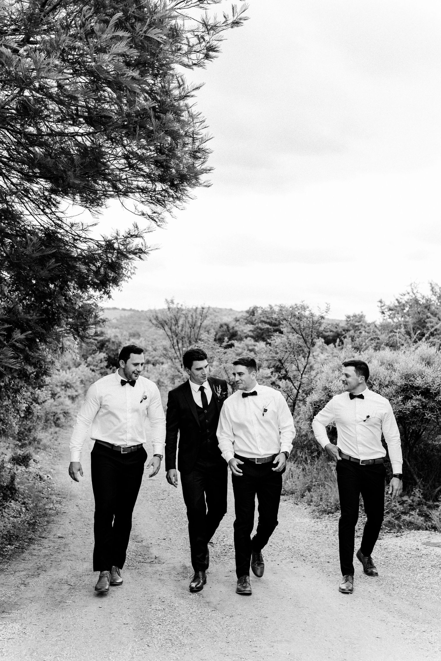 Wedding party walks together on outdoor path in black and white photography.