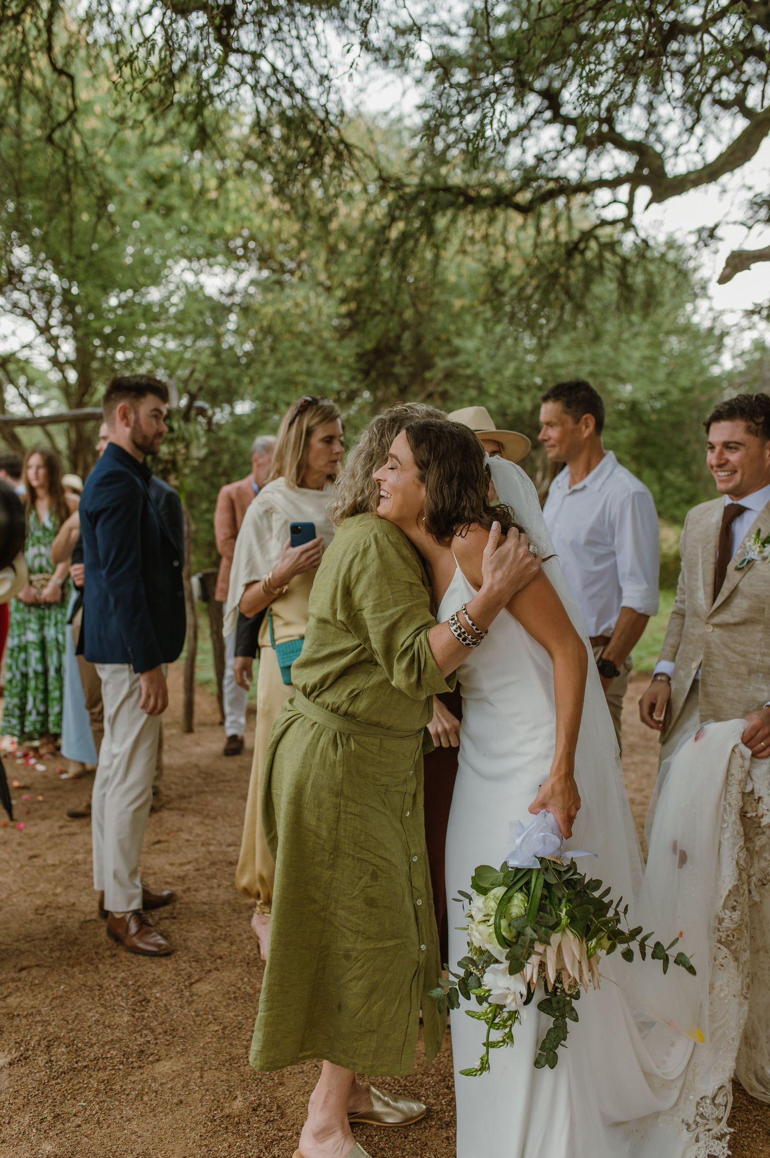 Wedding guests mingling and celebrating under trees at an outdoor reception.