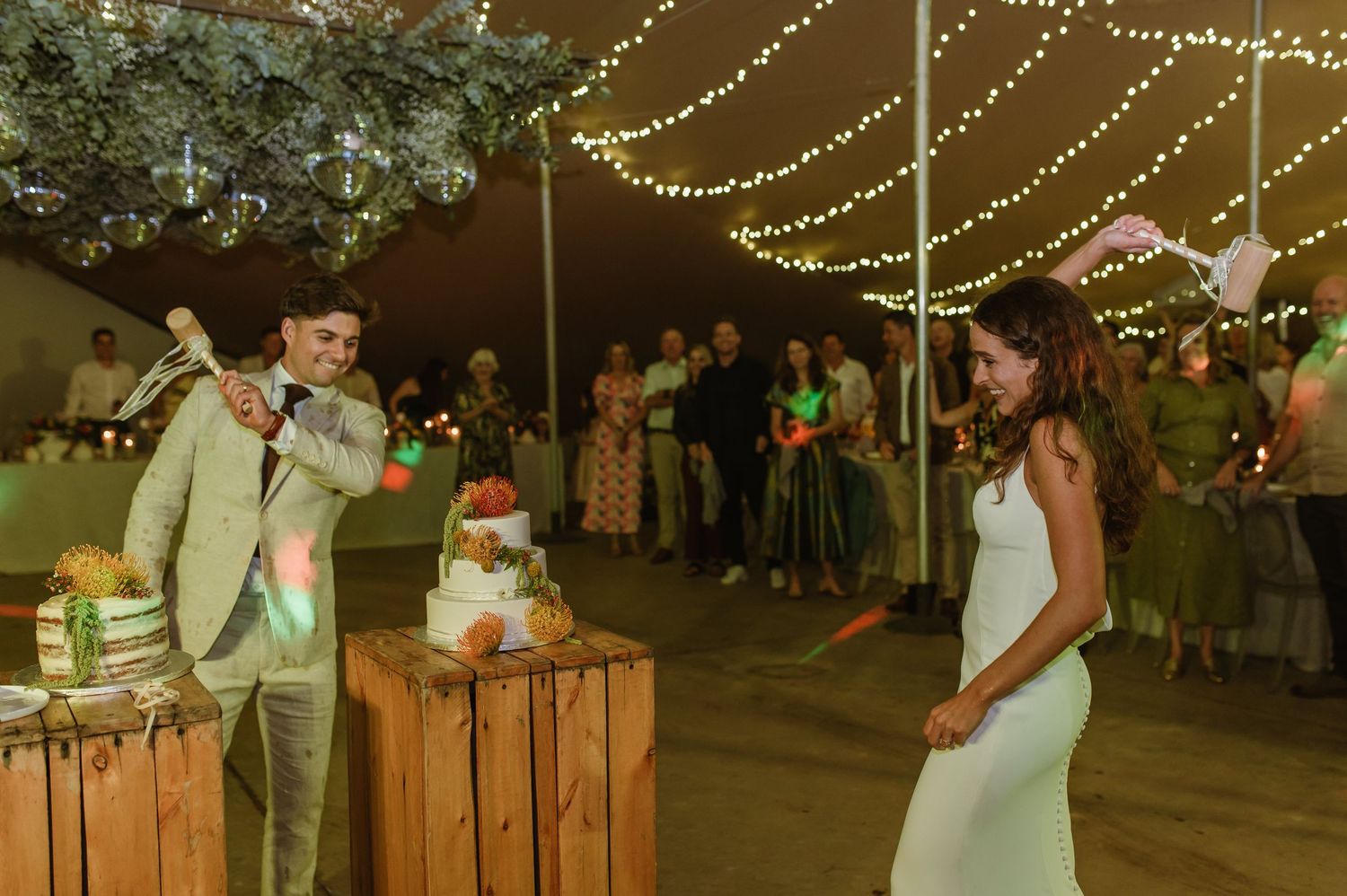 Wedding reception guests dance and celebrate under twinkling lights and tent canopy.