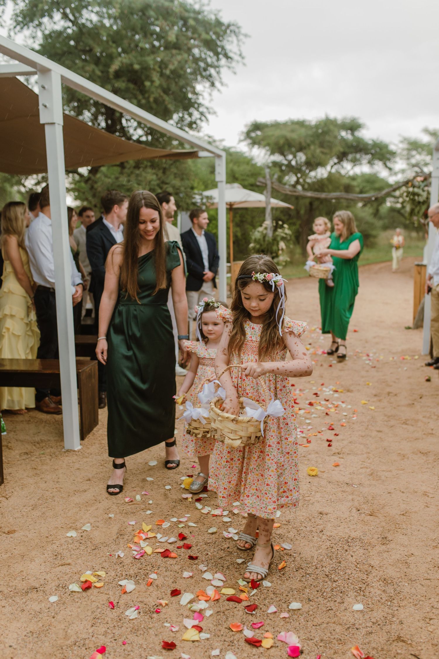 Young children scatter rose petals along a desert wedding aisle lined with white posts.