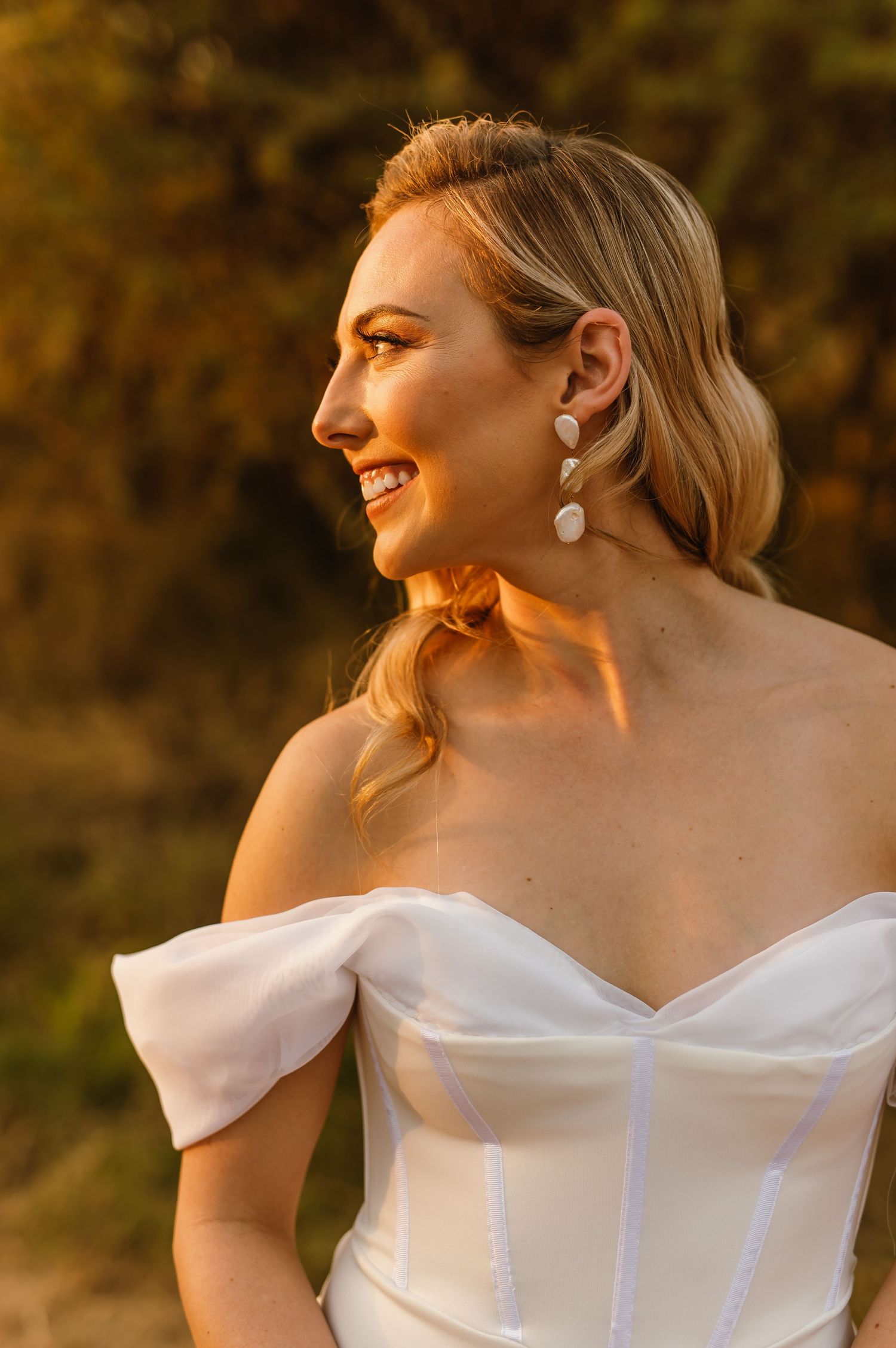 Close-up portrait of a bride wearing an elegant off-shoulder white wedding dress in warm golden light.