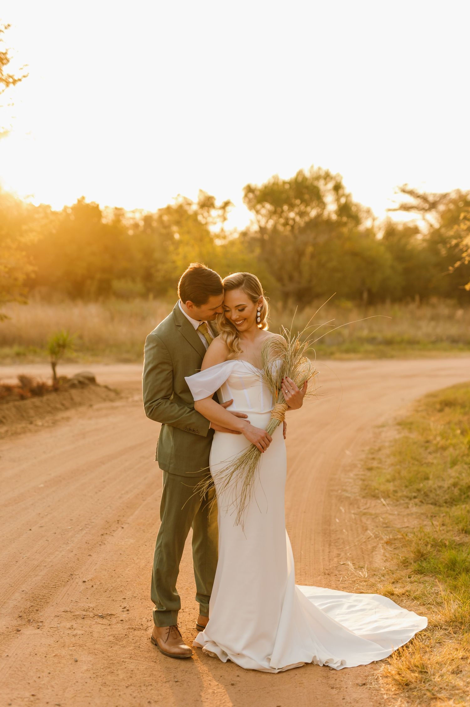 Wedding couple shares romantic moments on a sunlit dirt path during golden hour.