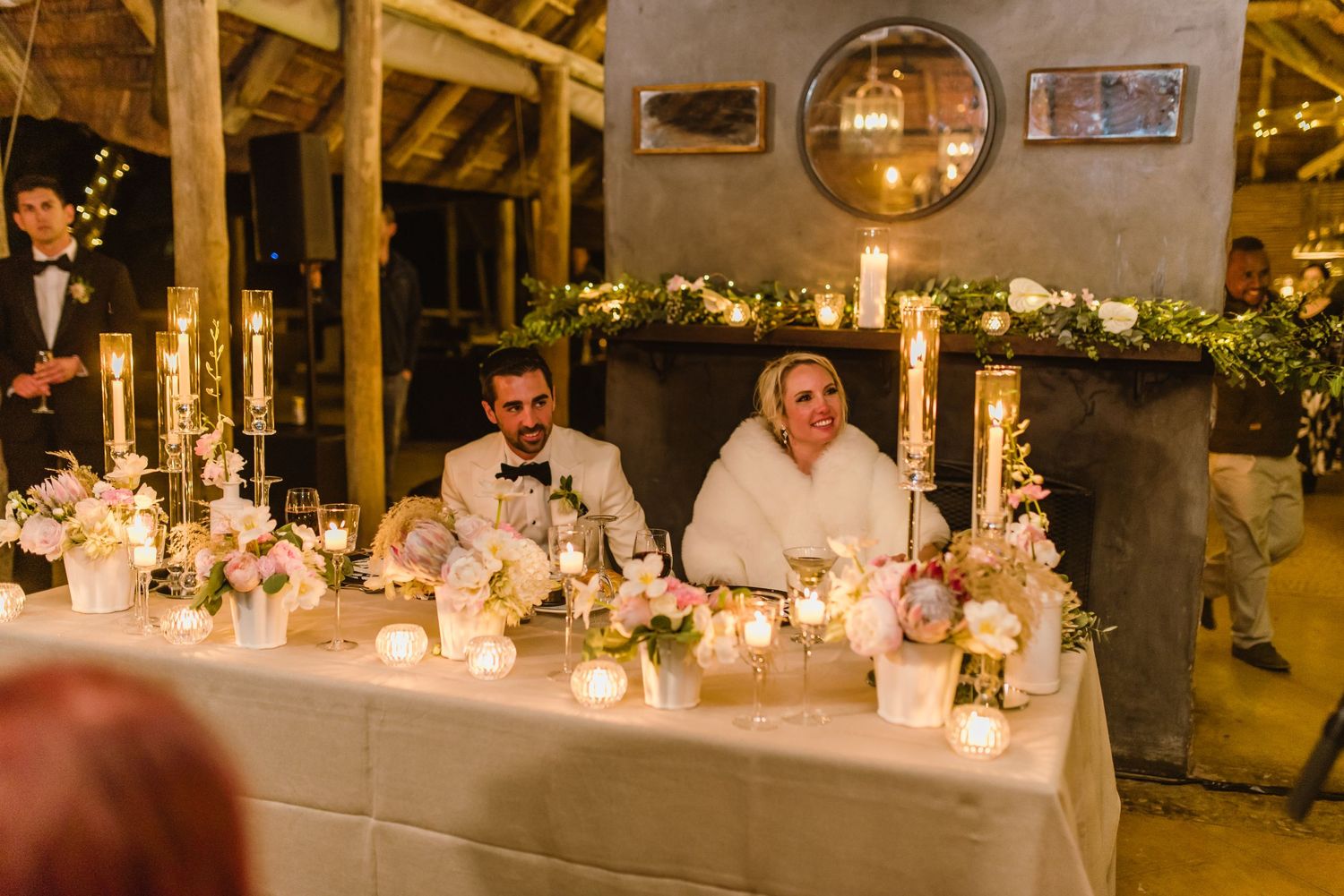 Newlyweds seated at a beautifully decorated head table with candles and floral arrangements.