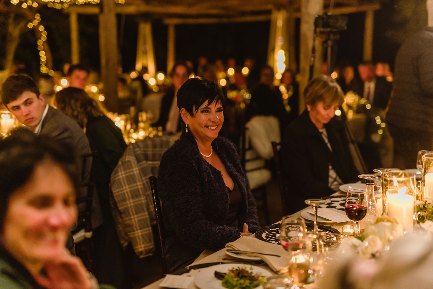 Wedding celebration with guests dining at elegantly decorated tables under warm lighting.
