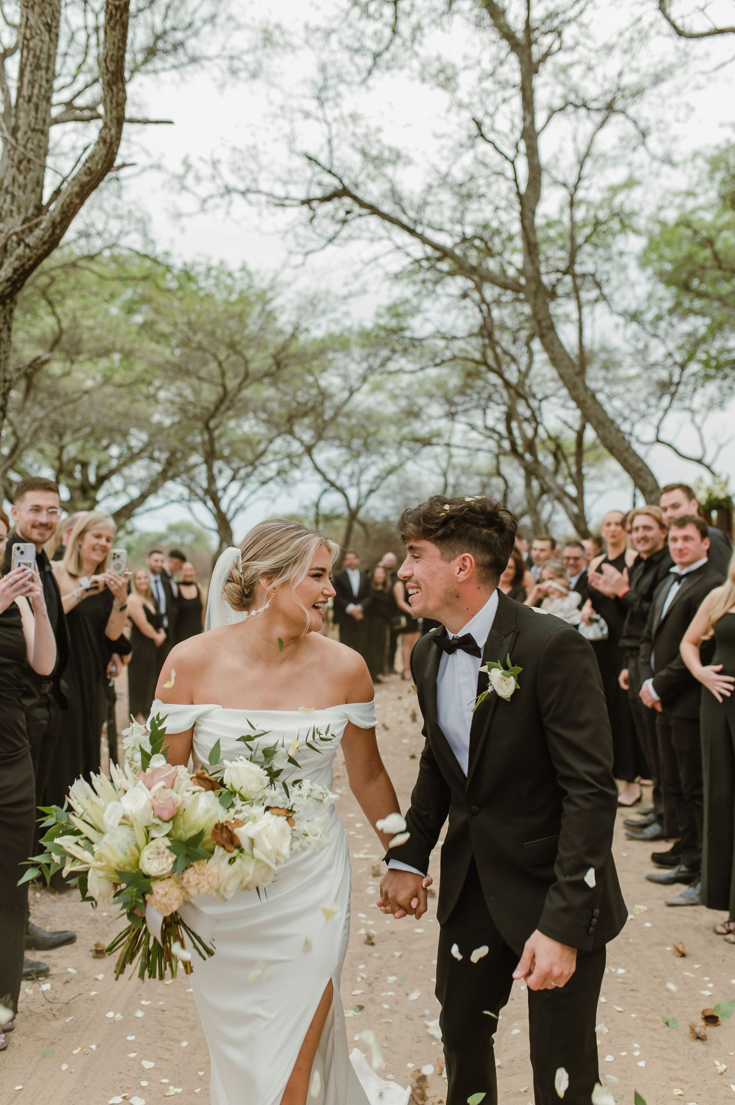 Elegant outdoor wedding celebration with guests in black attire throwing confetti.