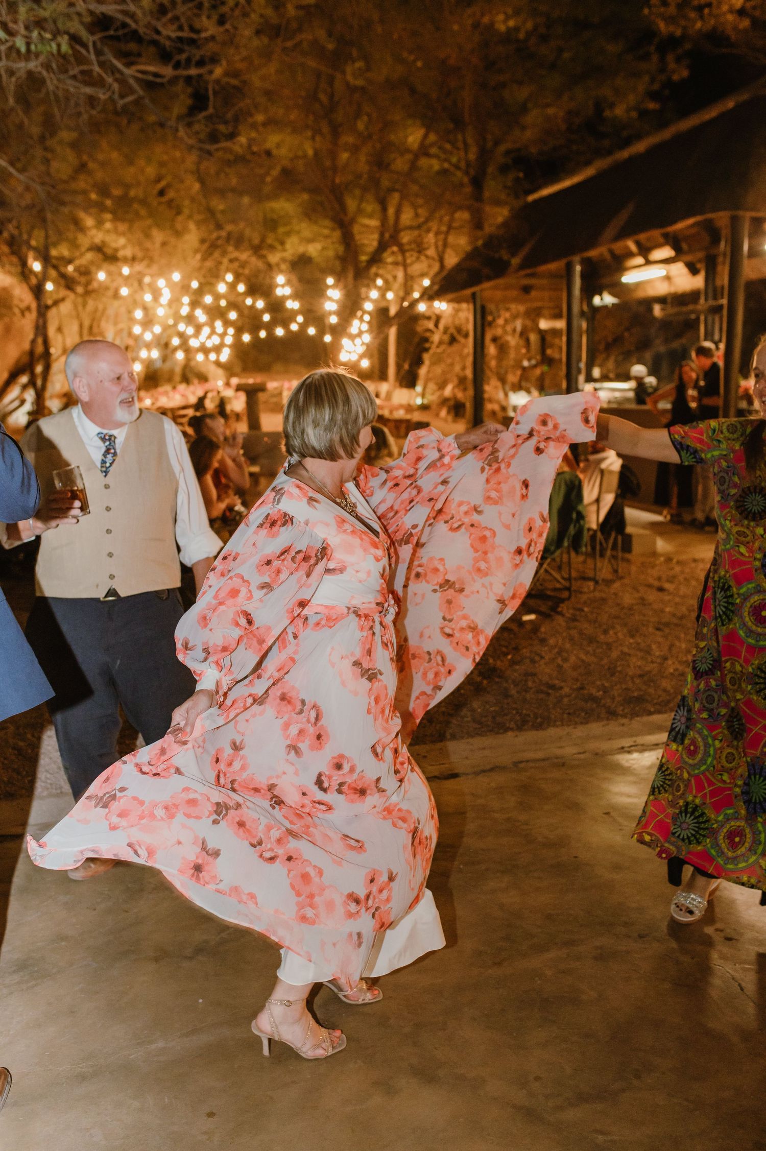 Guest in flowing floral dress dances under string lights at outdoor evening reception.