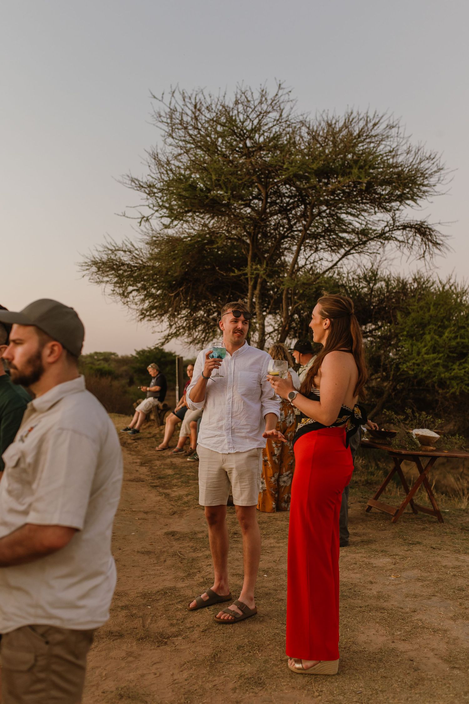 Group of people enjoying drinks and conversation at an outdoor gathering during sunset.