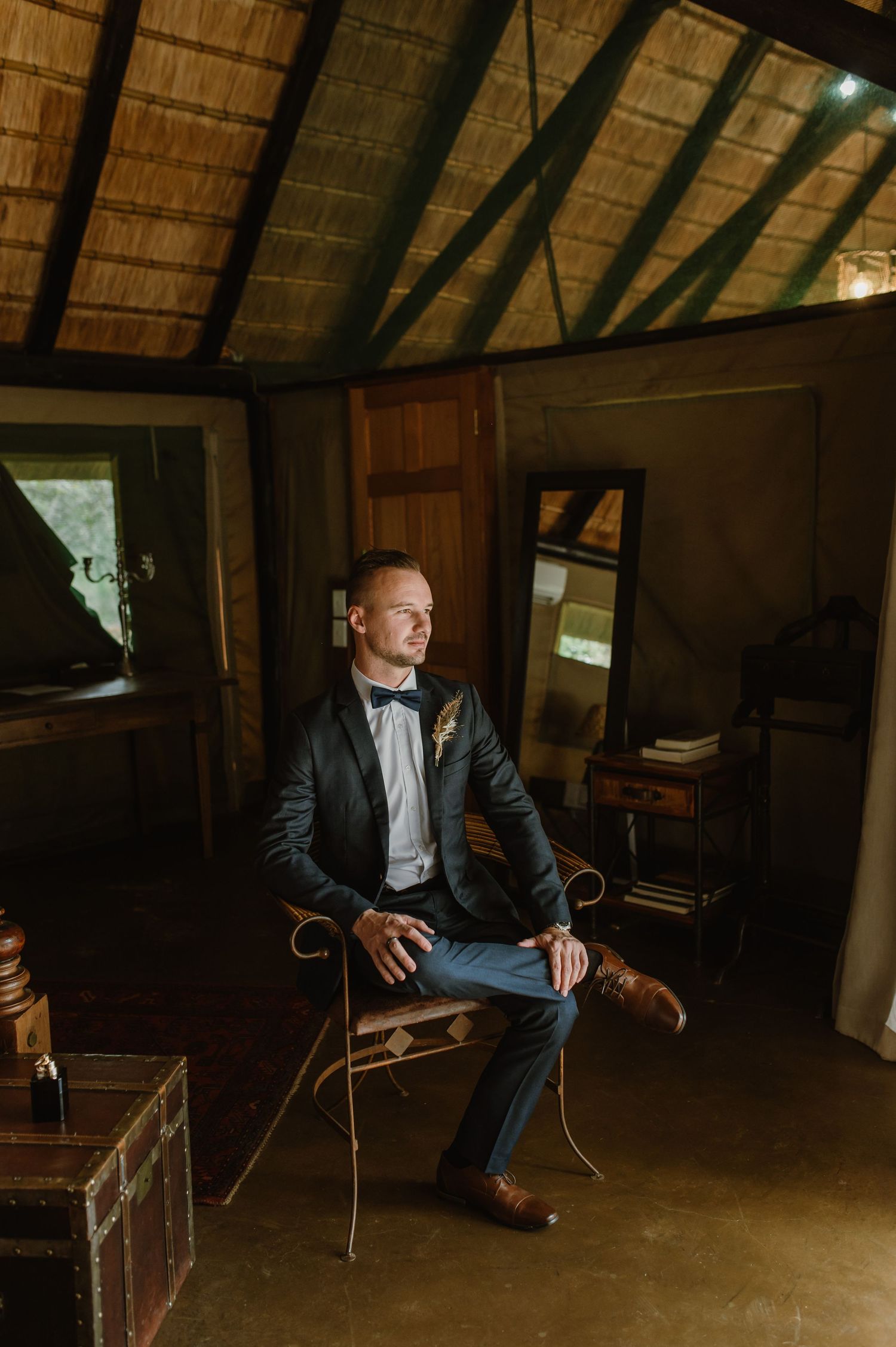 Person in dark suit posing in rustic room with dramatic lighting and wooden beams.