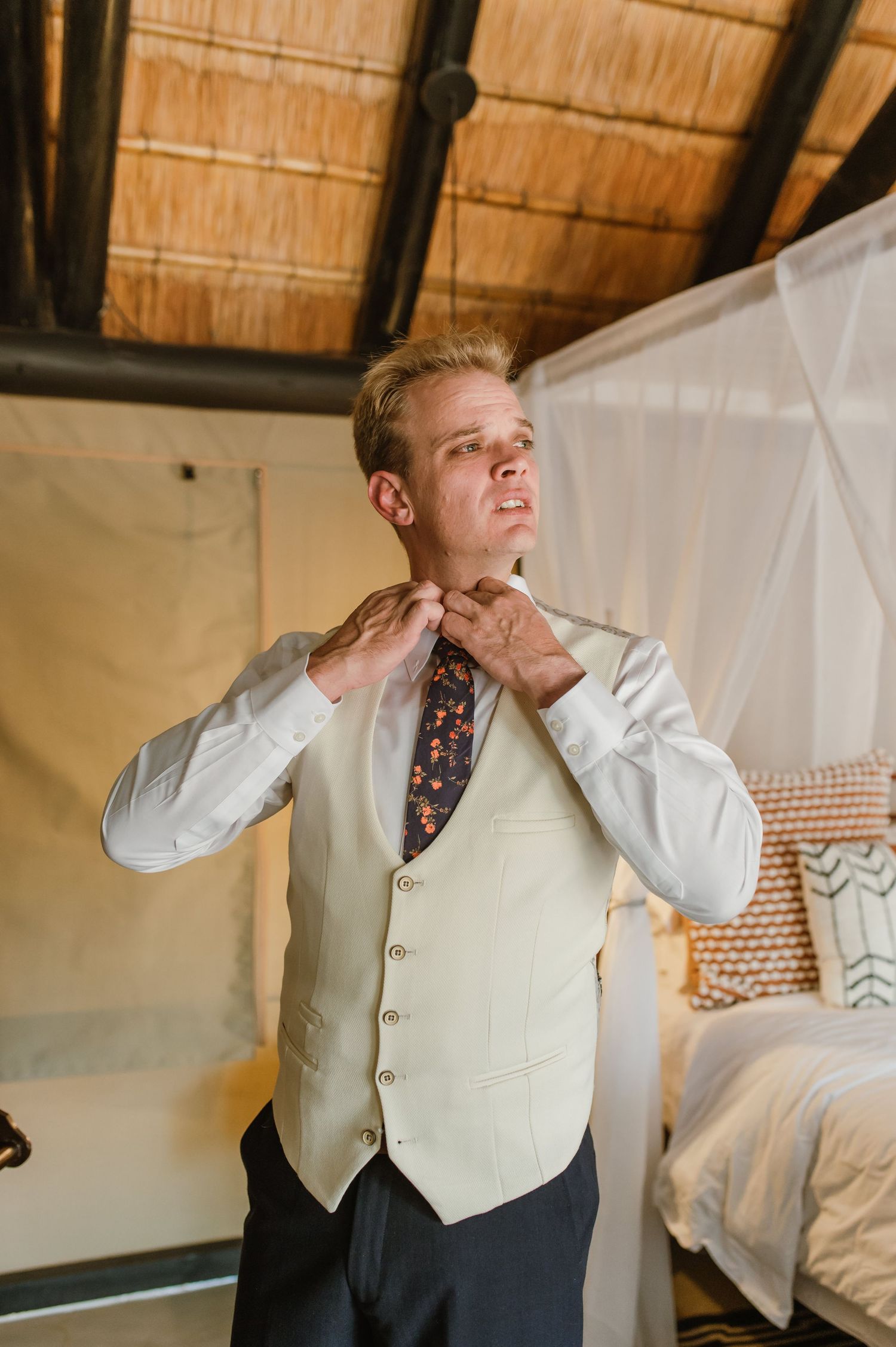 Person adjusting a floral tie while getting ready in a rustic-styled room.