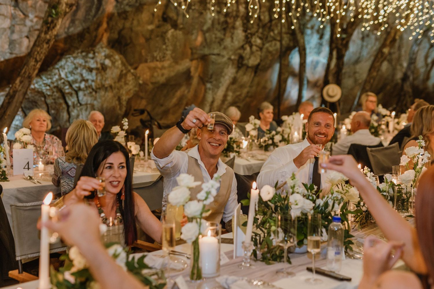Candlelit wedding reception tables decorated with white floral arrangements under string lights.