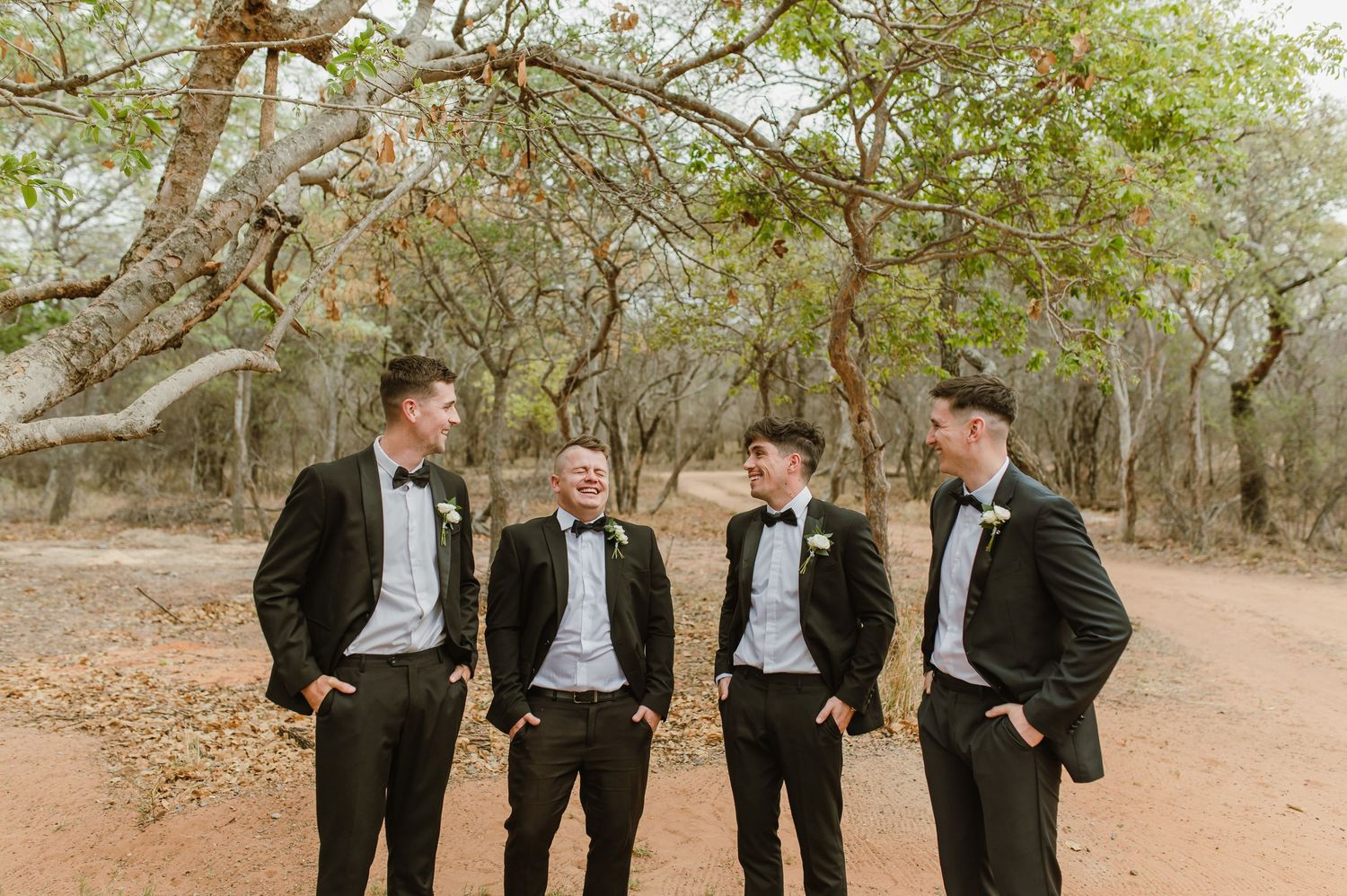 Wedding party in black tuxedos walking together through a natural outdoor setting.