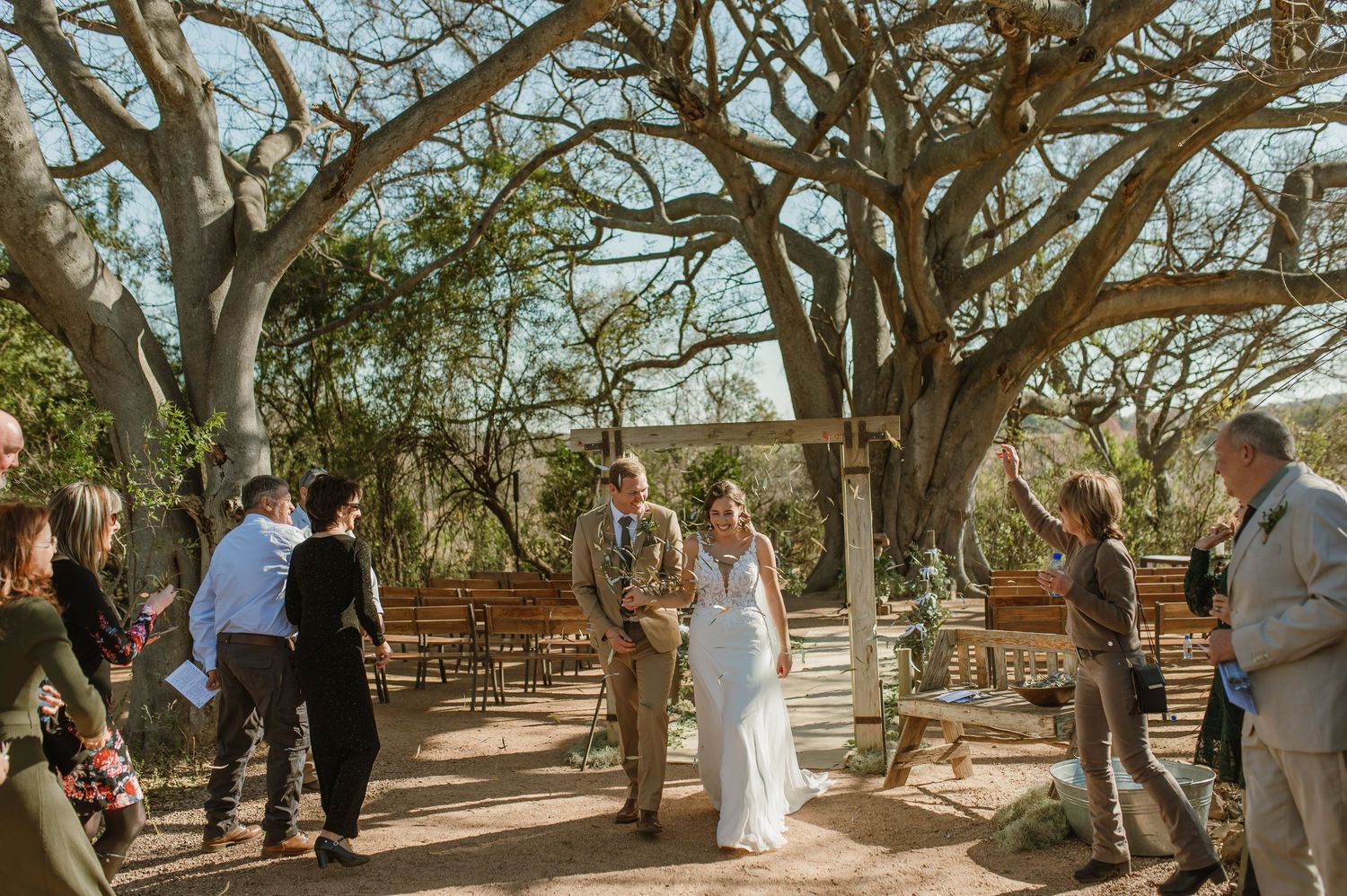 Wedding ceremony under a canopy of gnarled trees with guests gathered in an outdoor setting.